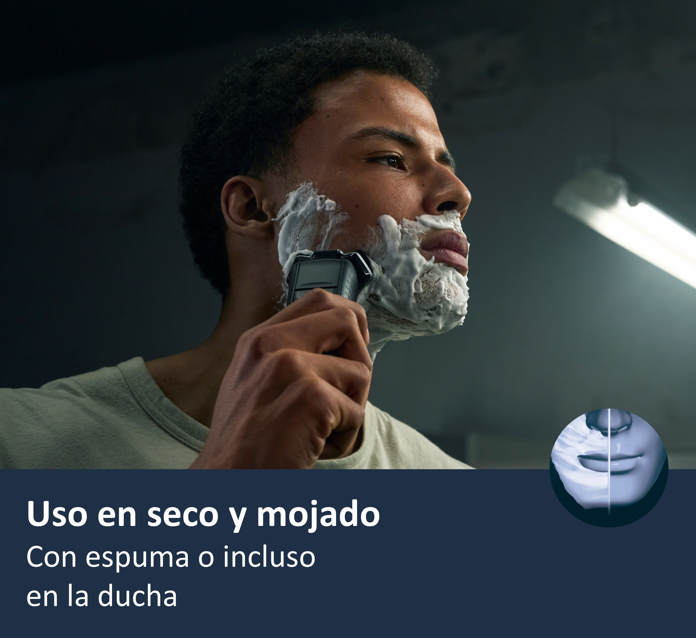 Hombre afeitándose con espuma y afeitadora eléctrica. Fondo oscuro.