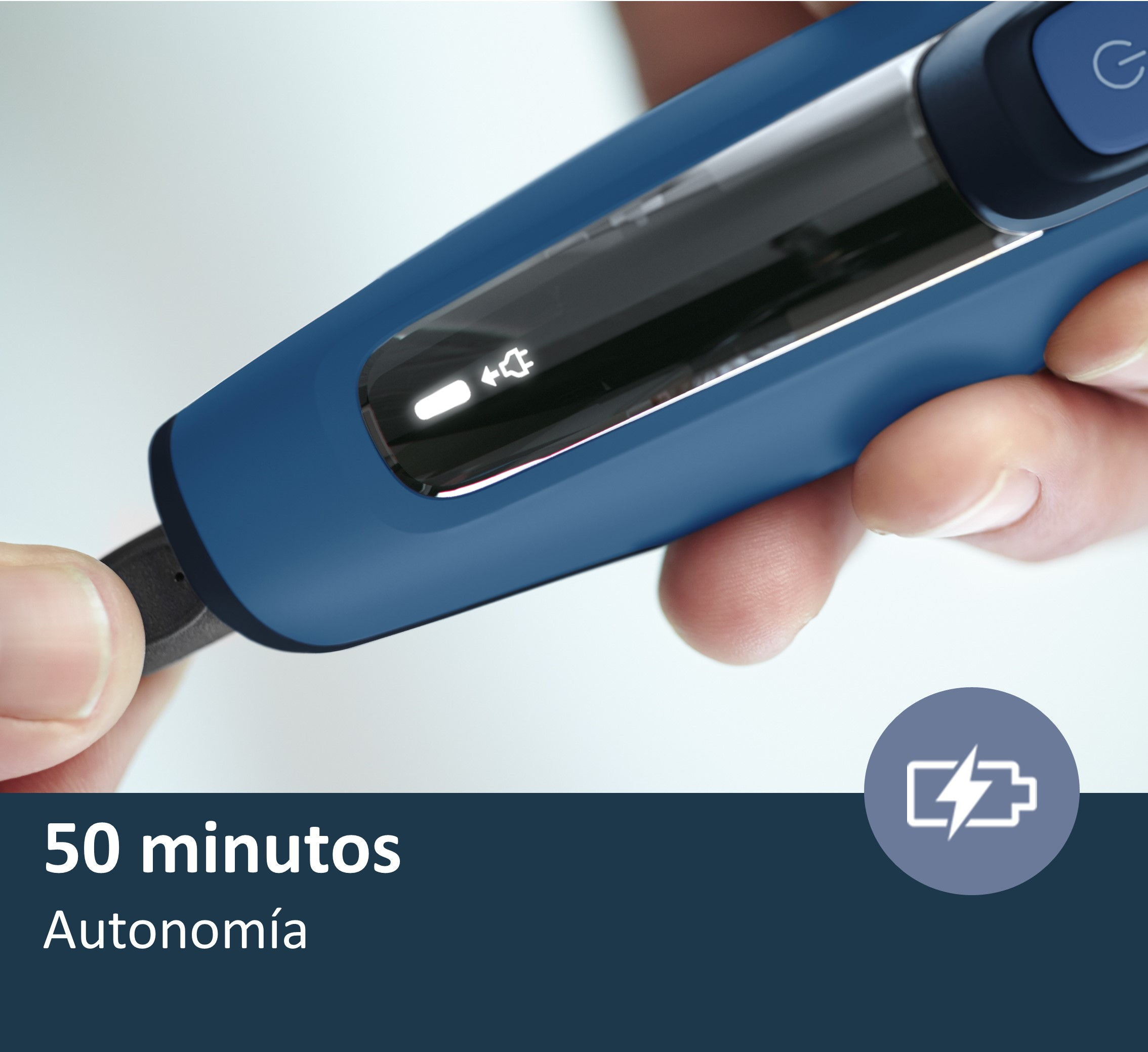 Una mano sosteniendo una afeitadora eléctrica azul y plateada con un cable de carga.