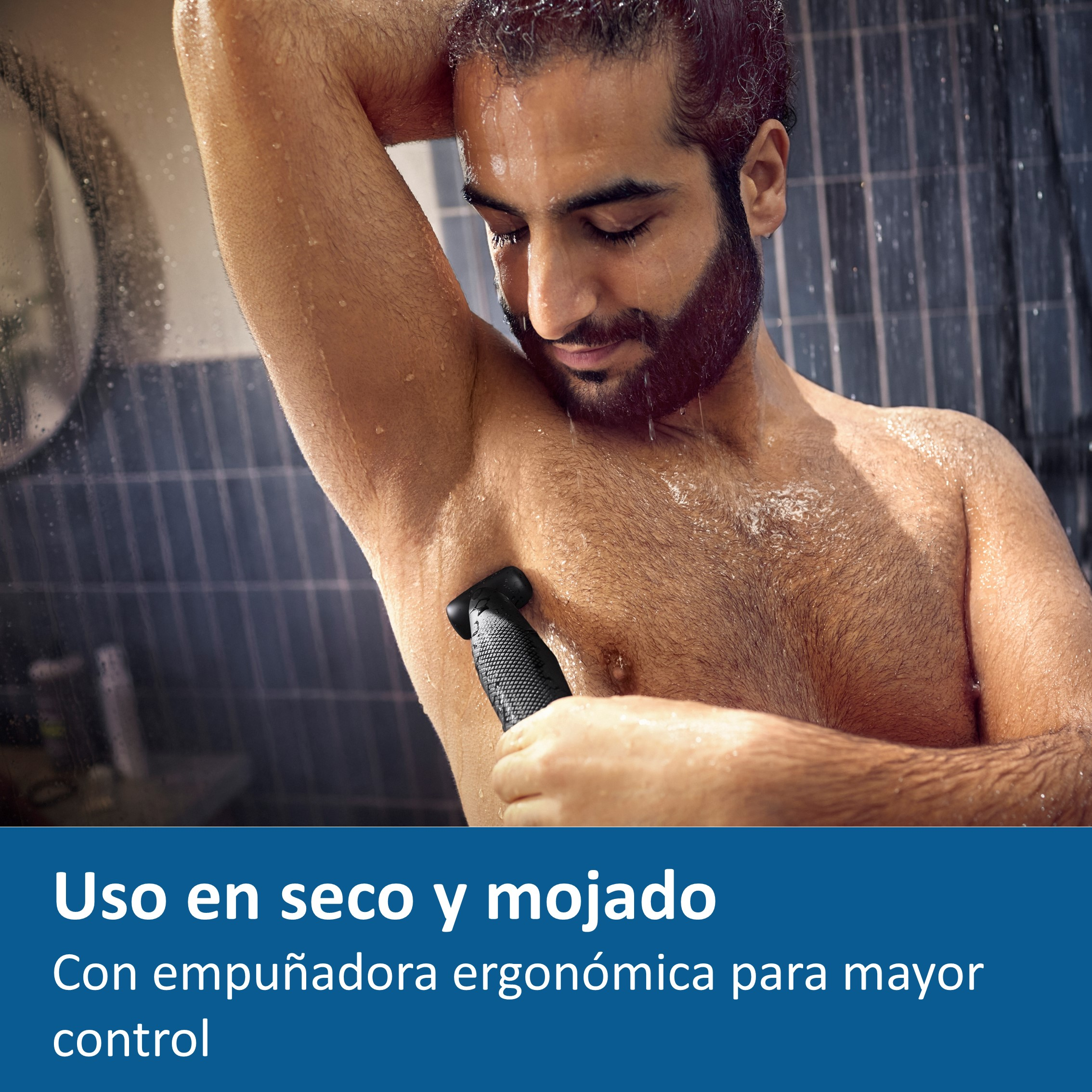 Hombre afeitándose la axila en la ducha con una recortadora. El fondo es una ducha.