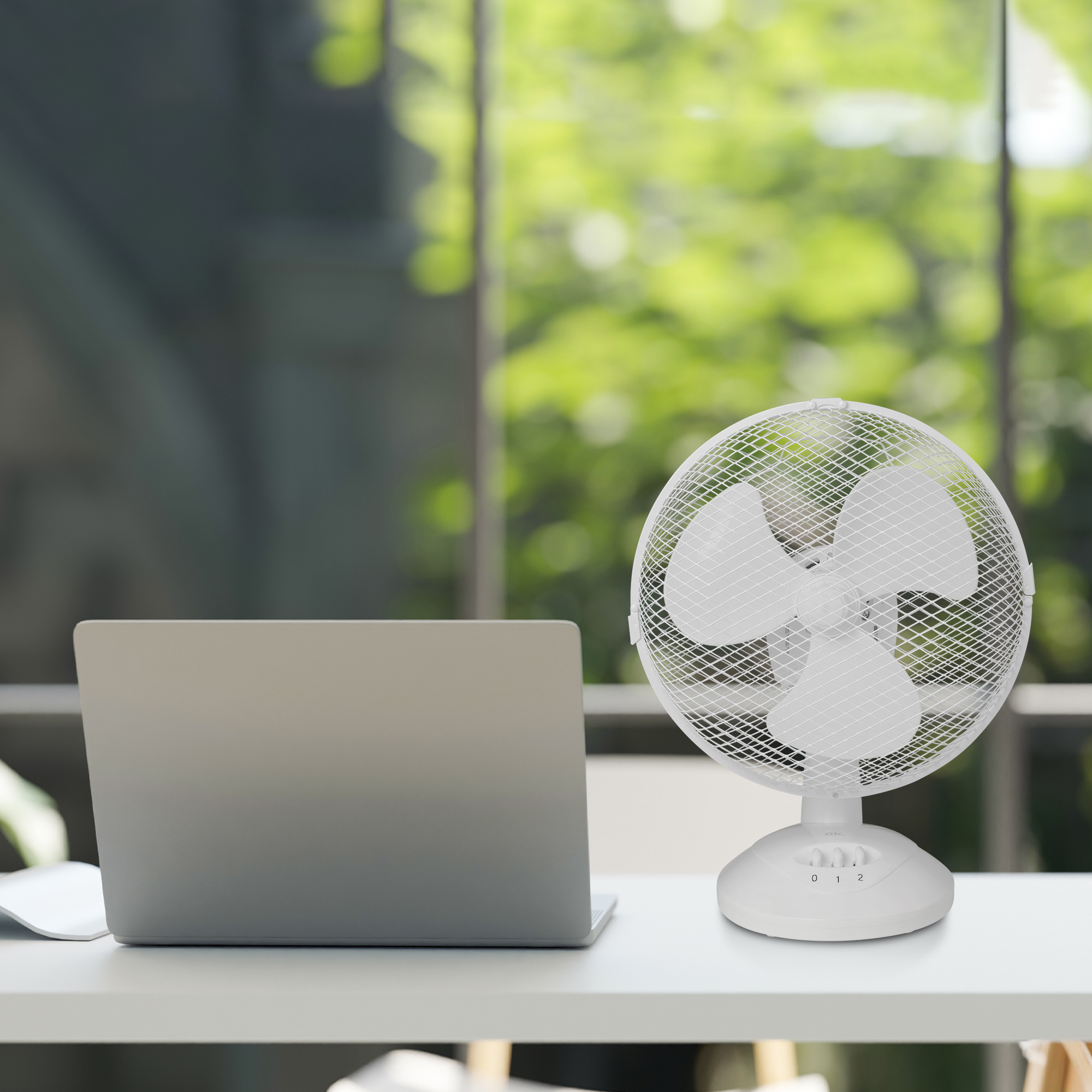 Biały wentylator na biurku w pobliżu laptopa.