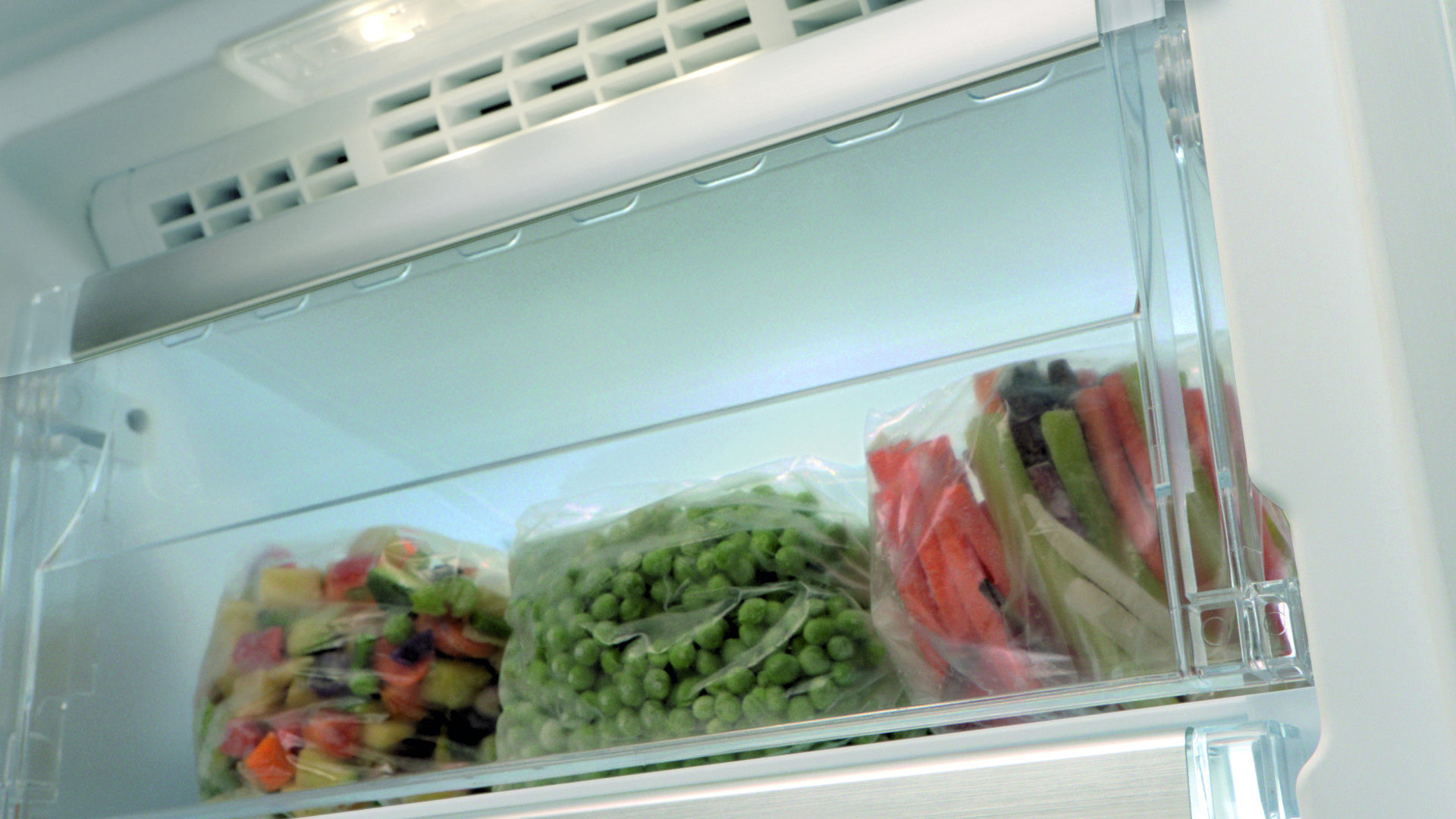 Interior de un refrigerador con bolsas de verduras congeladas. Zanahorias, guisantes y verduras mixtas son visibles.