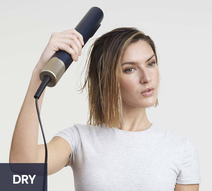 Frau benutzt einen marineblauen Haartrockner, schaut in die Kamera. Weißer Hintergrund, Text 'DRY'.