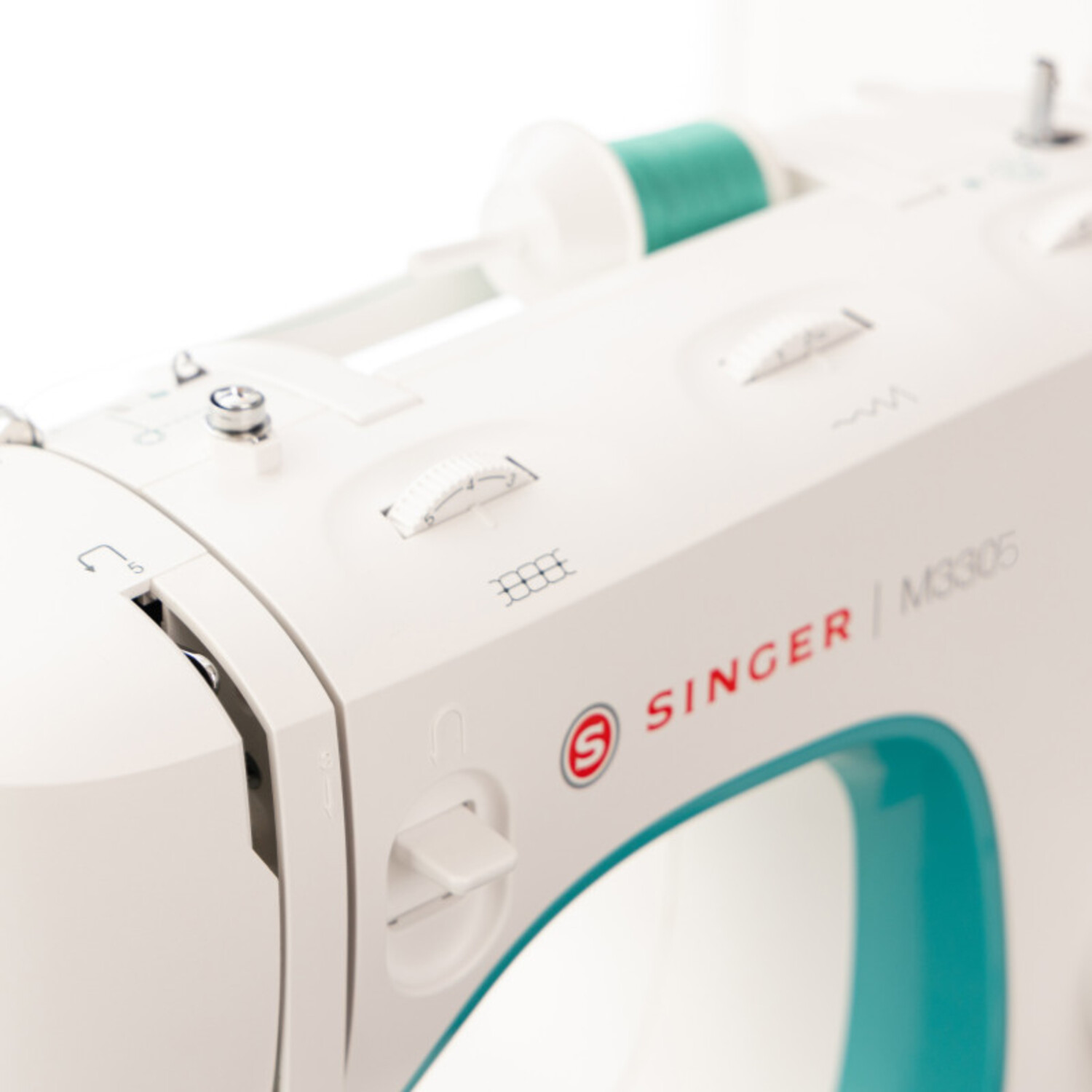 Machine à coudre blanche avec des accents turquoise, des bobines de fil, et des cadrans.