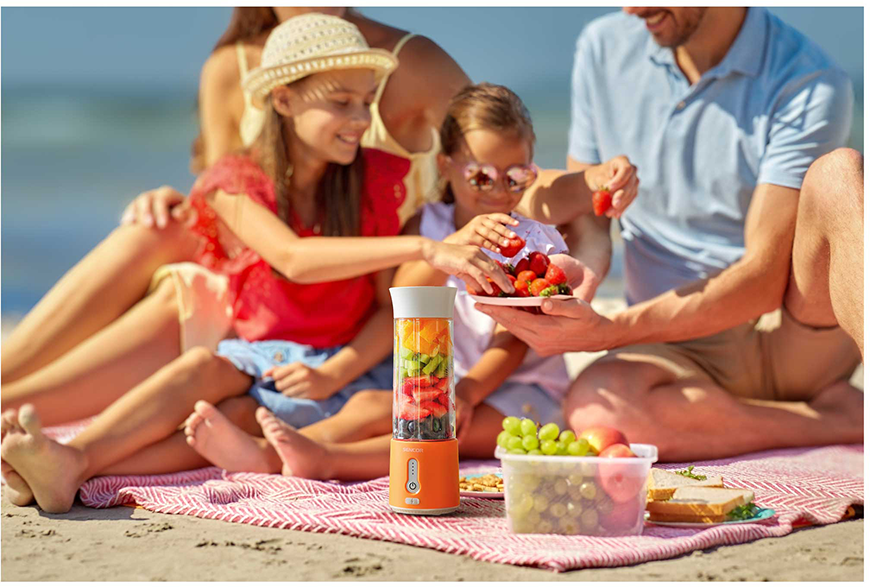 Egy család a strandon, egy turmixgéppel, ami smoothiet készít. Gyümölcsöt és egy rétegezett összetevőkből álló turmixgépet osztanak meg.