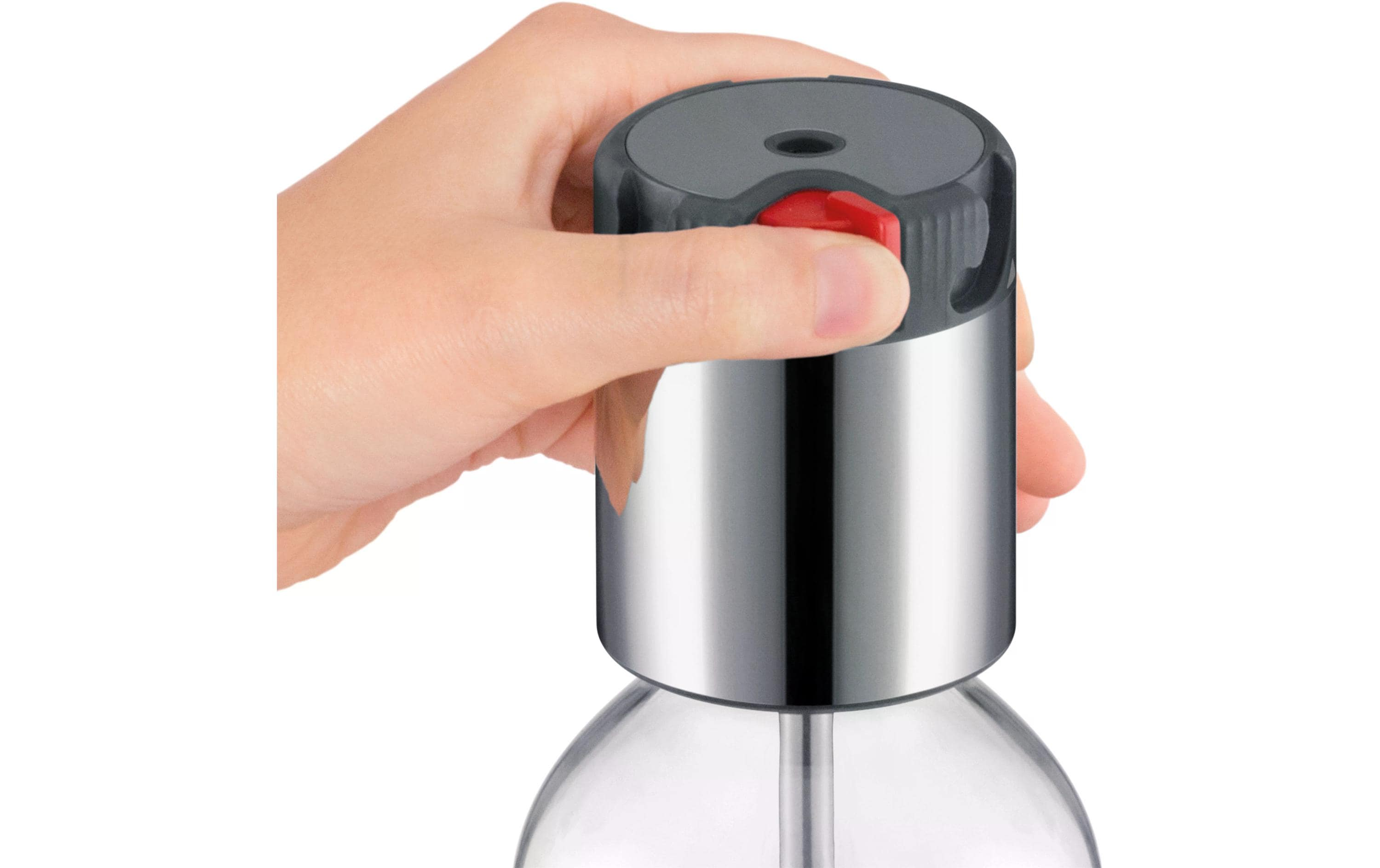 Eine Hand drückt einen roten Knopf auf einem silbernen und durchsichtigen Gerät, möglicherweise einem Soda-Maker.