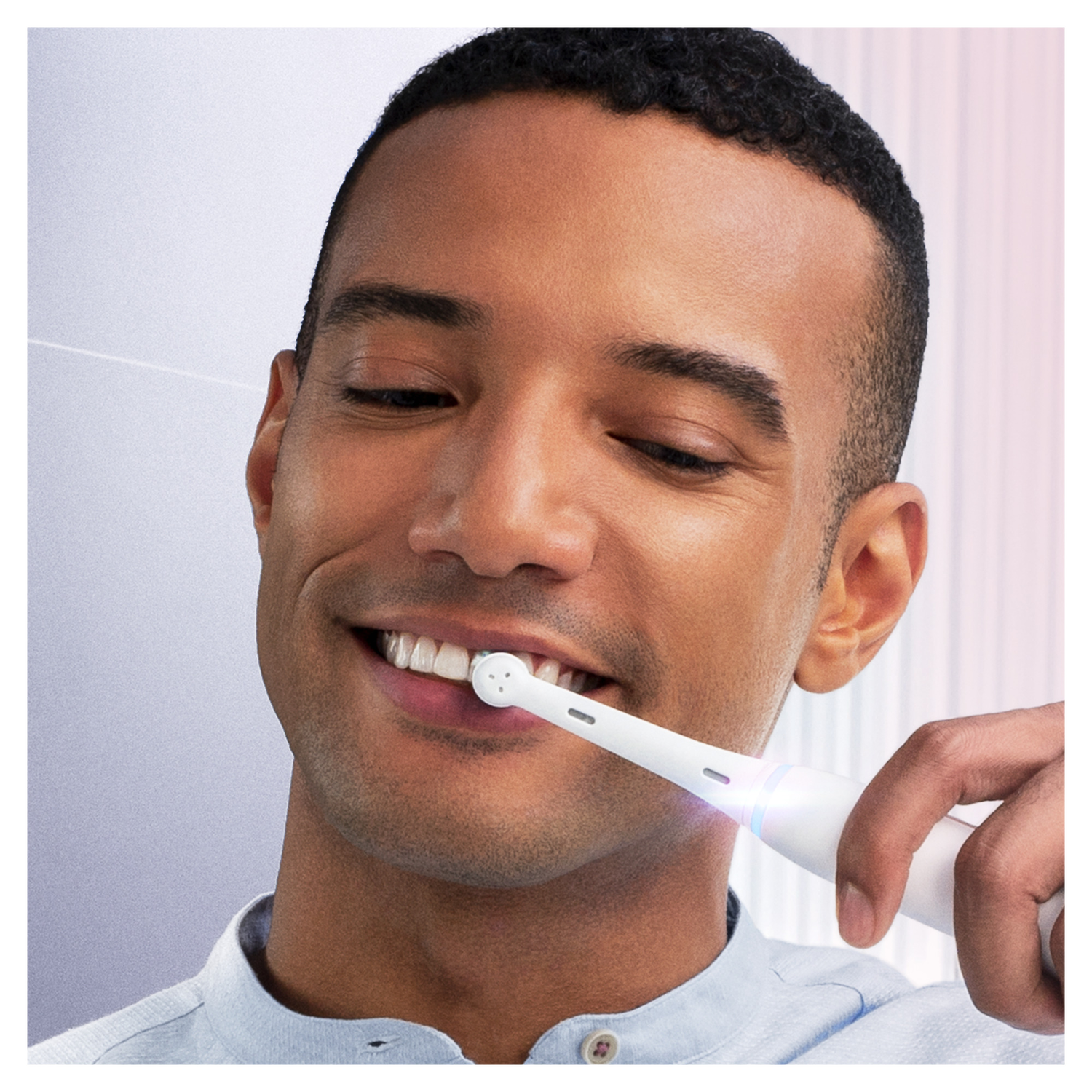 Man brushing teeth with an electric toothbrush, smiling with a light blue shirt.
