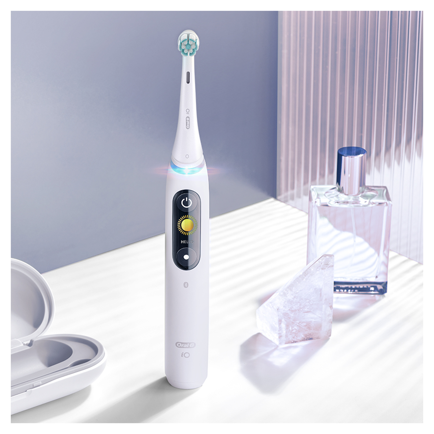 White electric toothbrush on a white surface with perfume and a crystal.