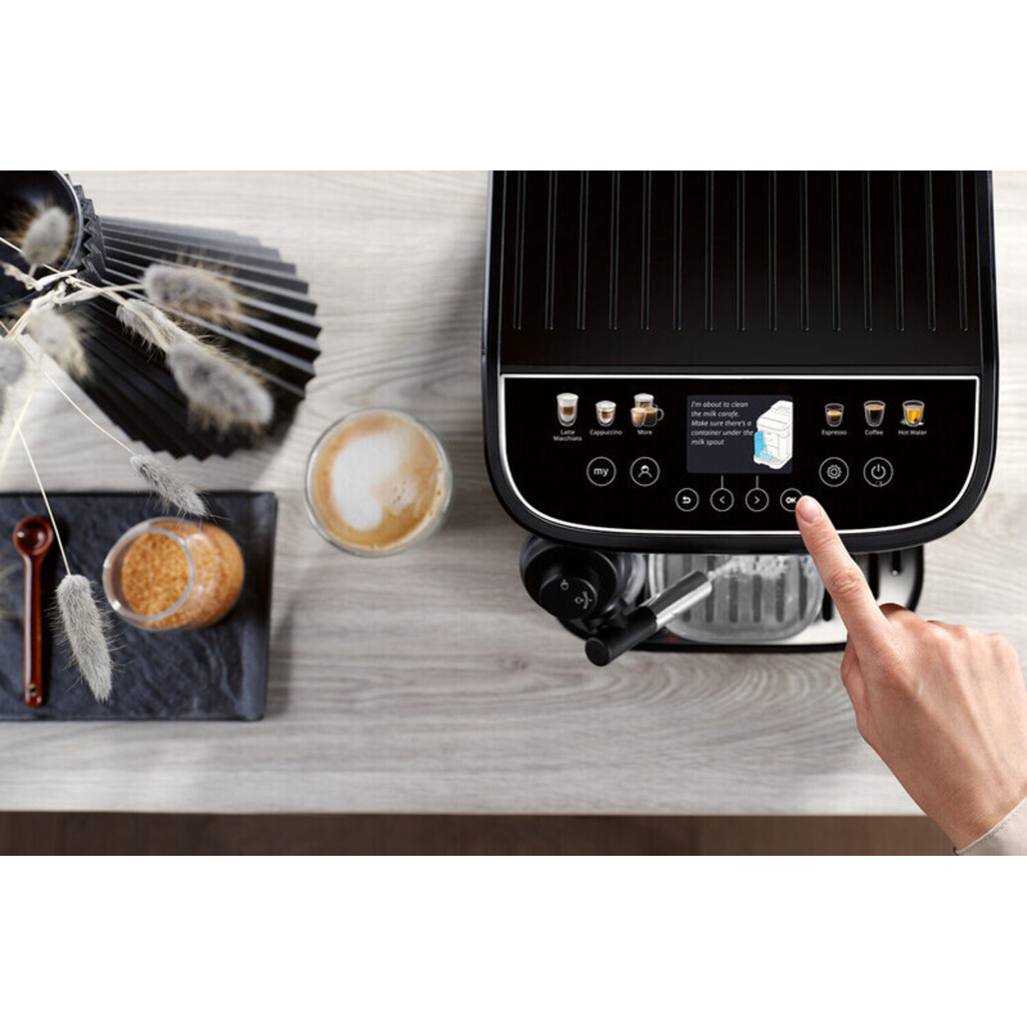 Coffee machine with cup, sugar, and a hand pressing a button.