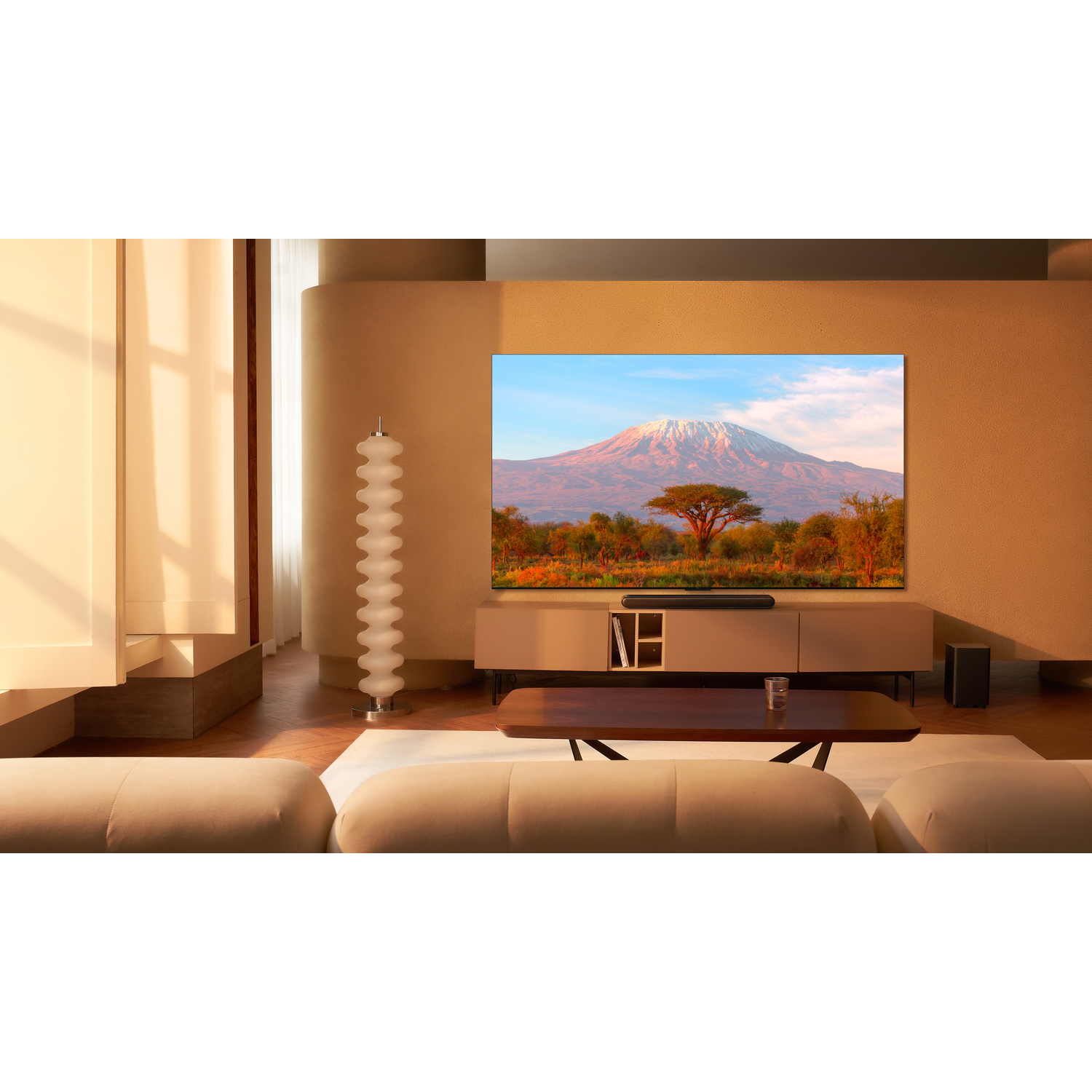 Woonkamer met grote tv die een berg toont. Beige muren en meubels.