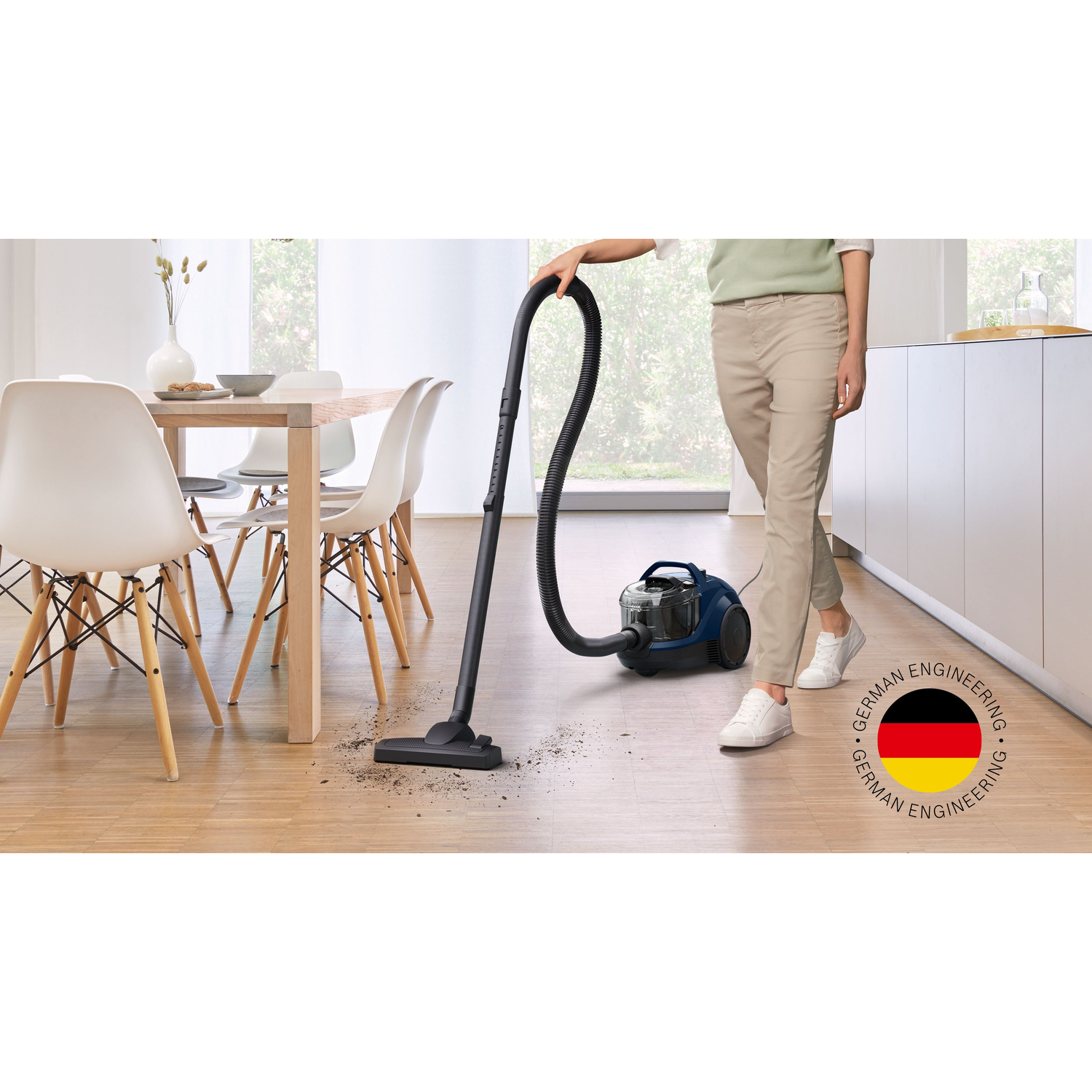 A person vacuums a wooden floor. A vacuum cleaner with a long black hose is used.