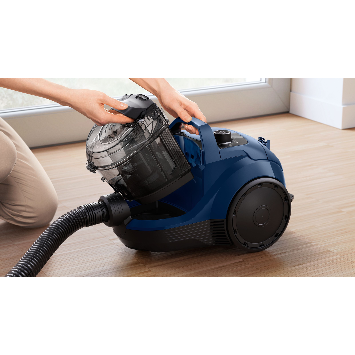 A person removing a canister from a blue vacuum cleaner.