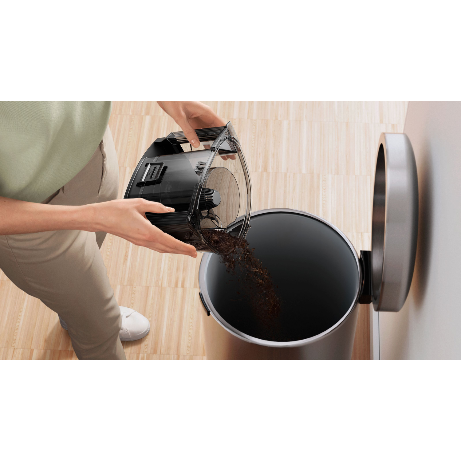 A person emptying a black vacuum cleaner container into a trash can.