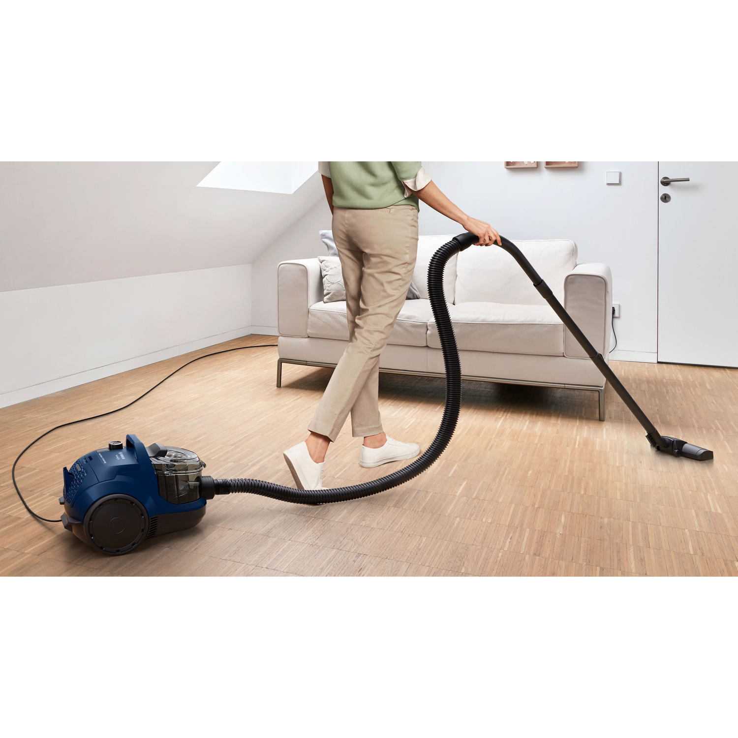 A woman vacuums a wooden floor. A blue vacuum cleaner is on the floor.