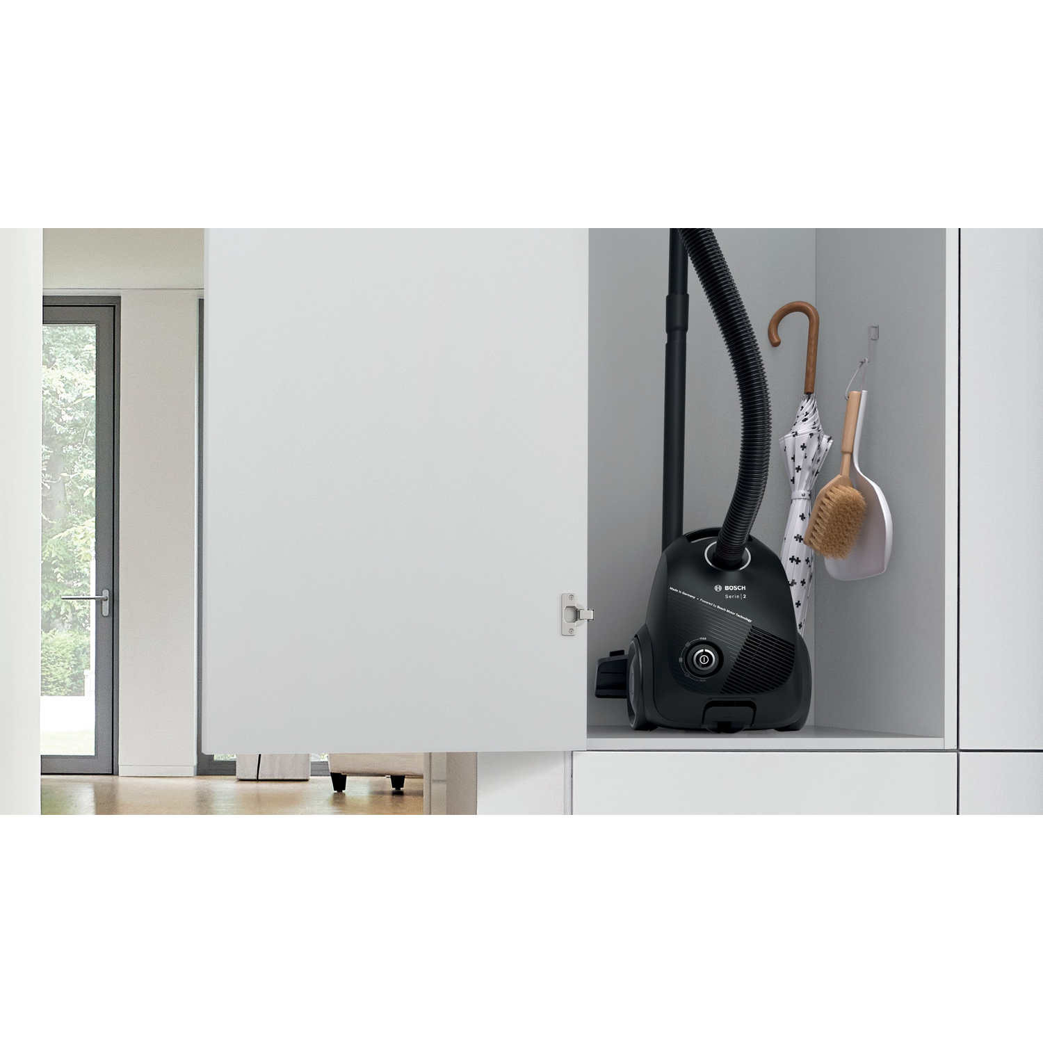 Opened white cabinet with a black vacuum cleaner, brush, and umbrella hanging inside.