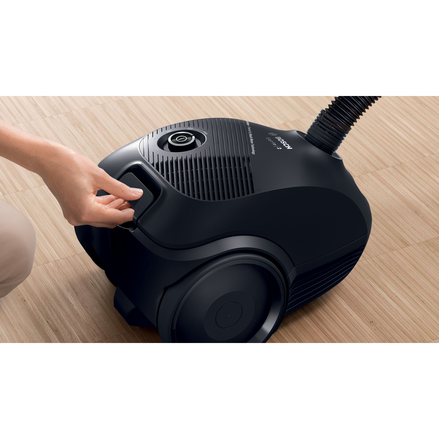 A black Bosch vacuum cleaner, a hand is opening the lid of the dust compartment.