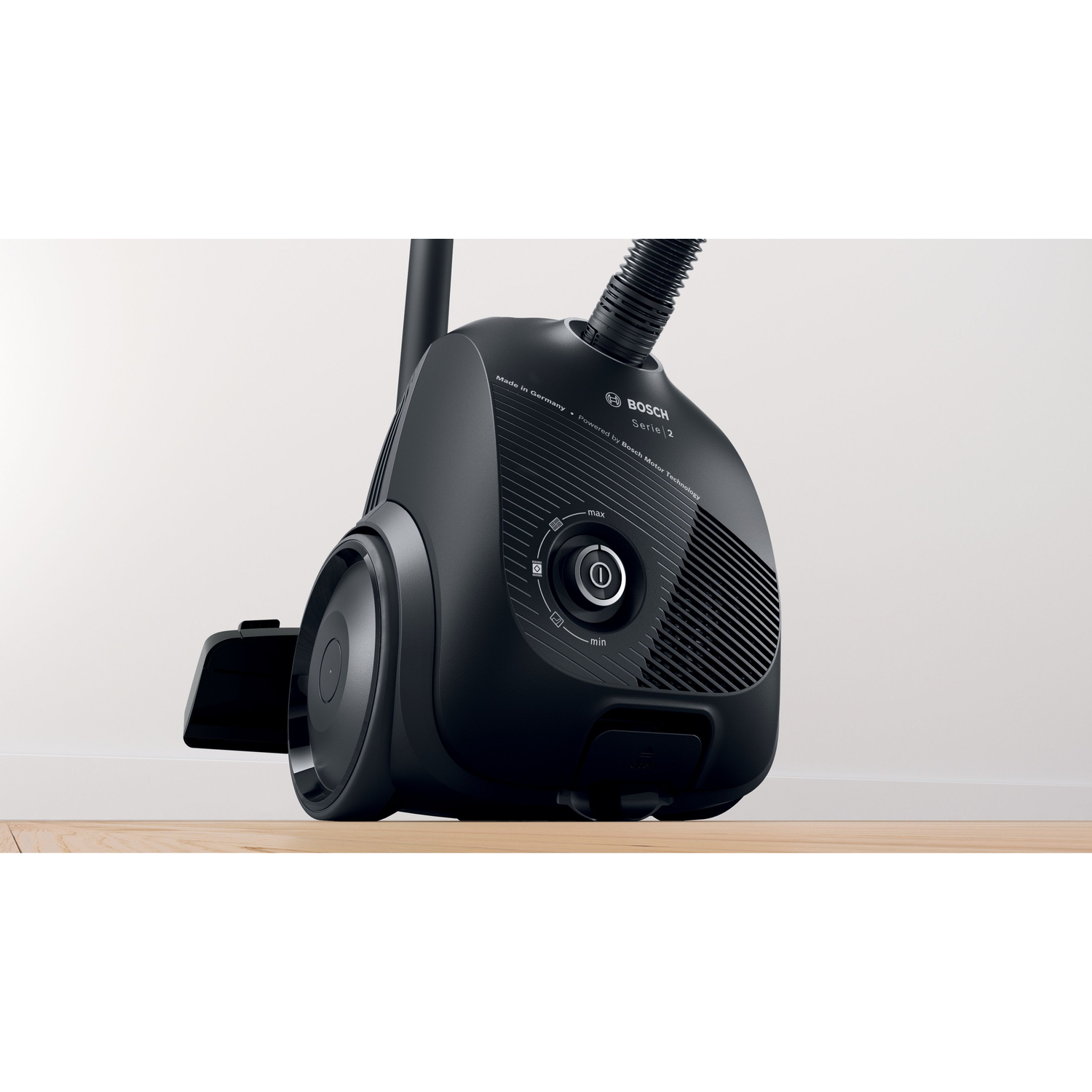 A black vacuum cleaner with a hose and a wheel, set on a wooden floor.
