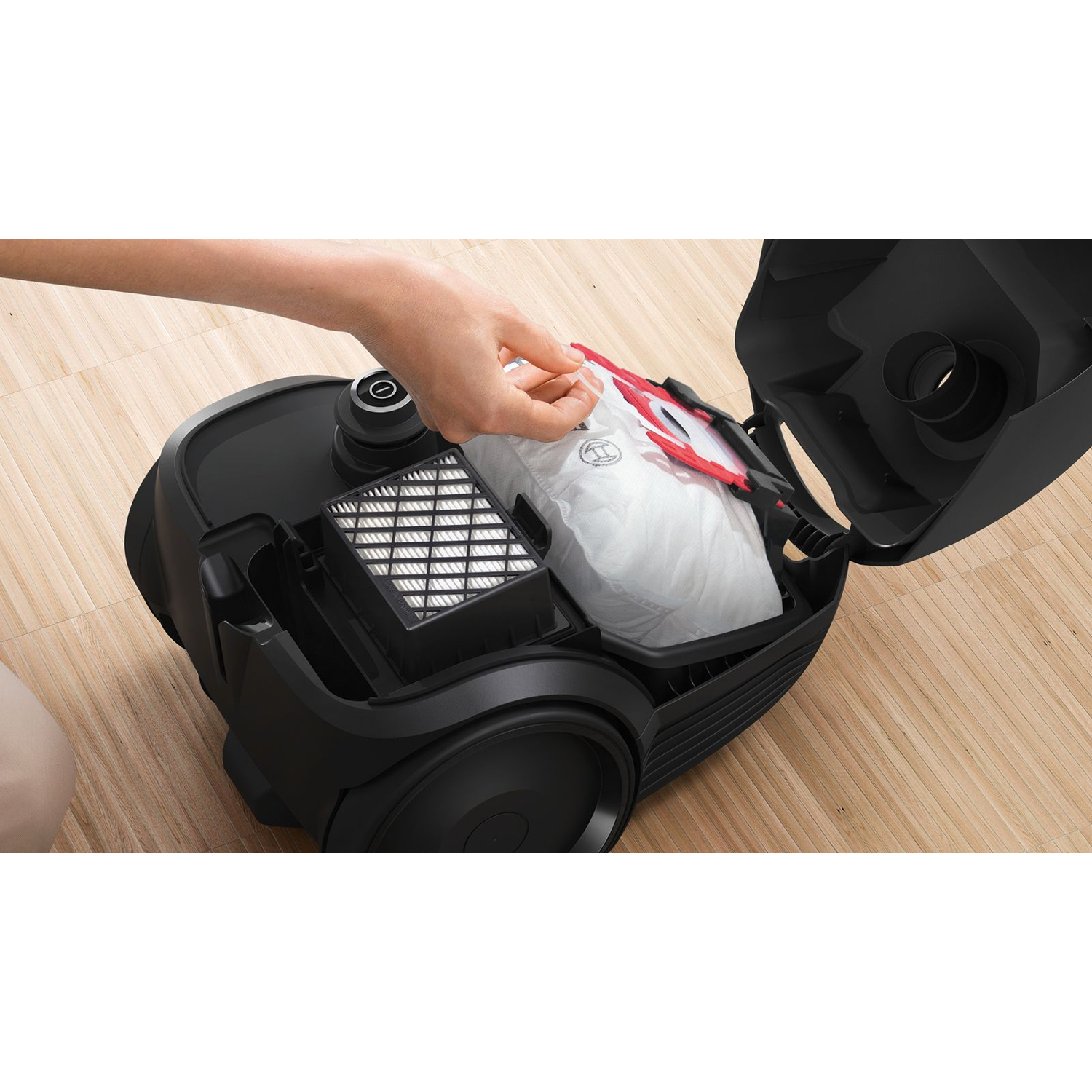 A hand holding a white vacuum bag, inside a black vacuum cleaner.