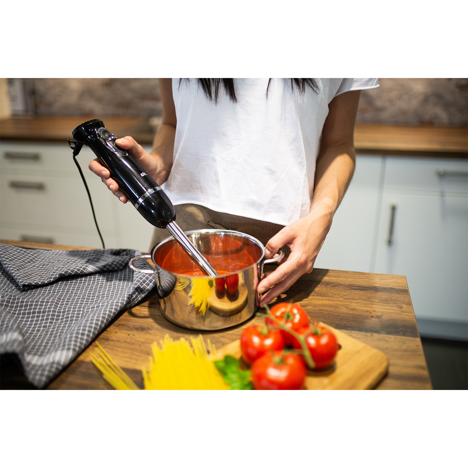 Donna che frulla salsa di pomodoro in una pentola con un frullatore a immersione, ingredienti vicini.
