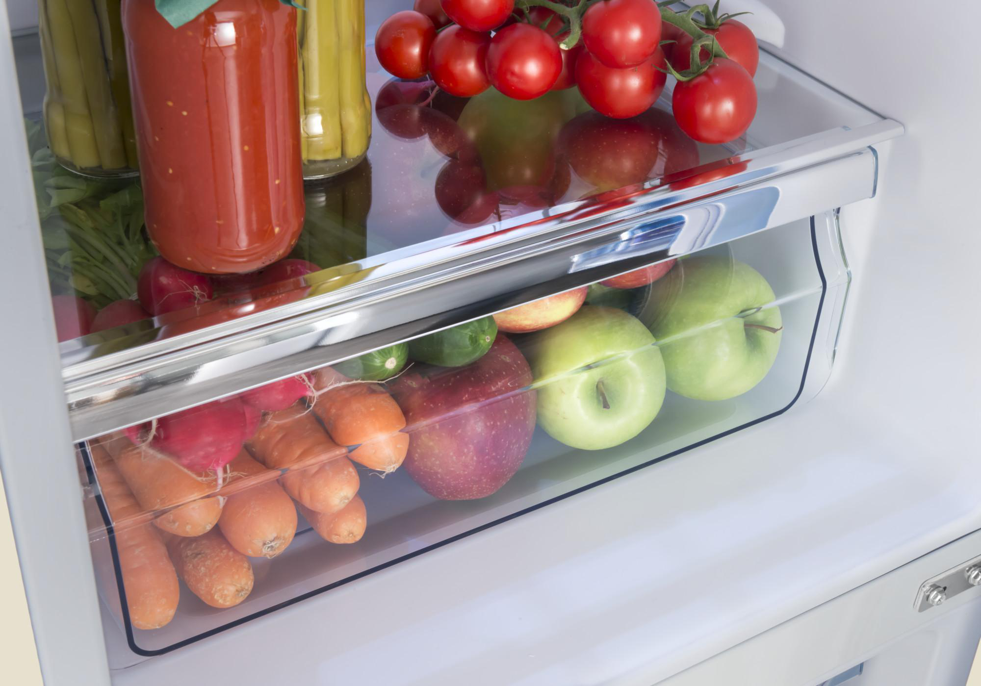 Eine Kühlschublade mit frischen Produkten, darunter Tomaten, Äpfel, Karotten und Gurken.