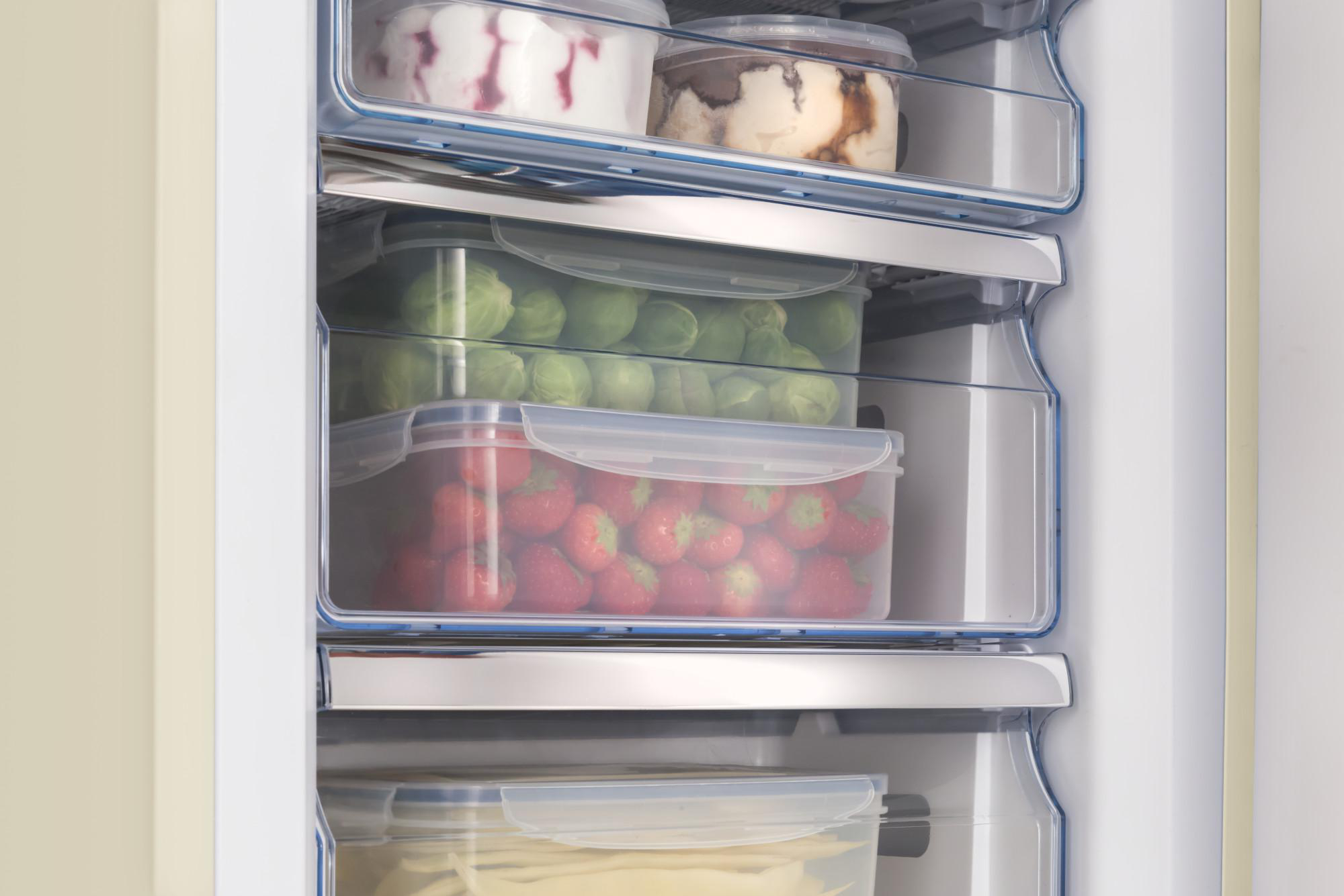 Nahaufnahme des Kühlschrankinnenraums mit Regalen mit Lebensmittelbehältern, darunter Eis und Erdbeeren.