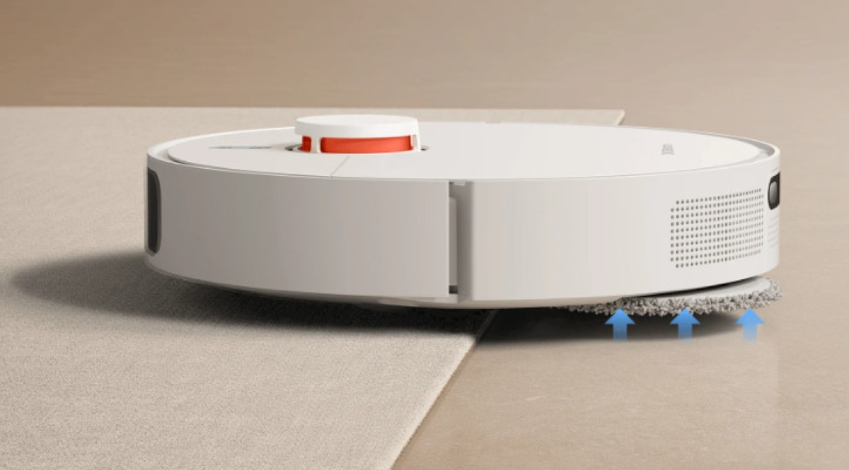 Biały odkurzacz automatyczny na dywanie, czyszczący krawędź. Tło to jasna podłoga.