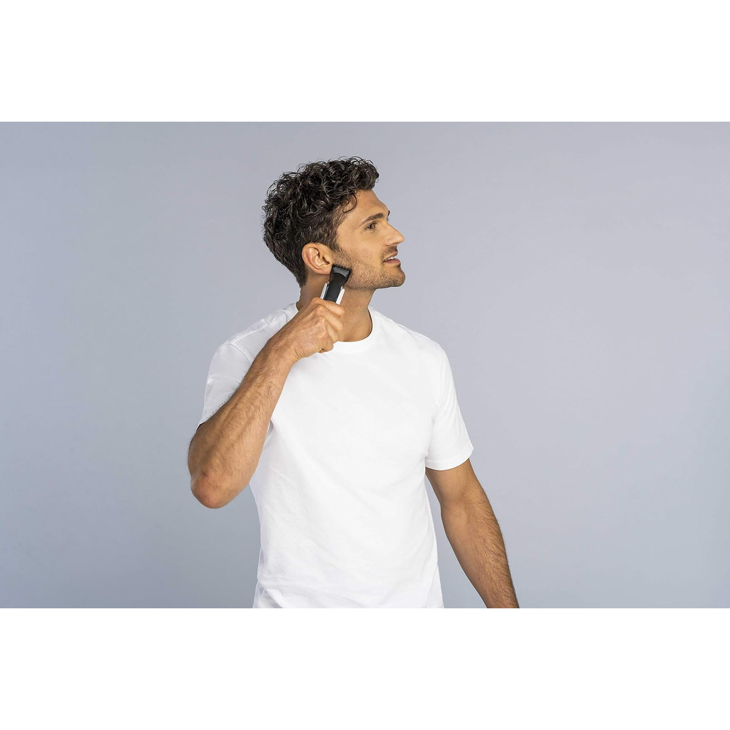 Un uomo con una camicia bianca si rade la barba con un rifinitore nero.