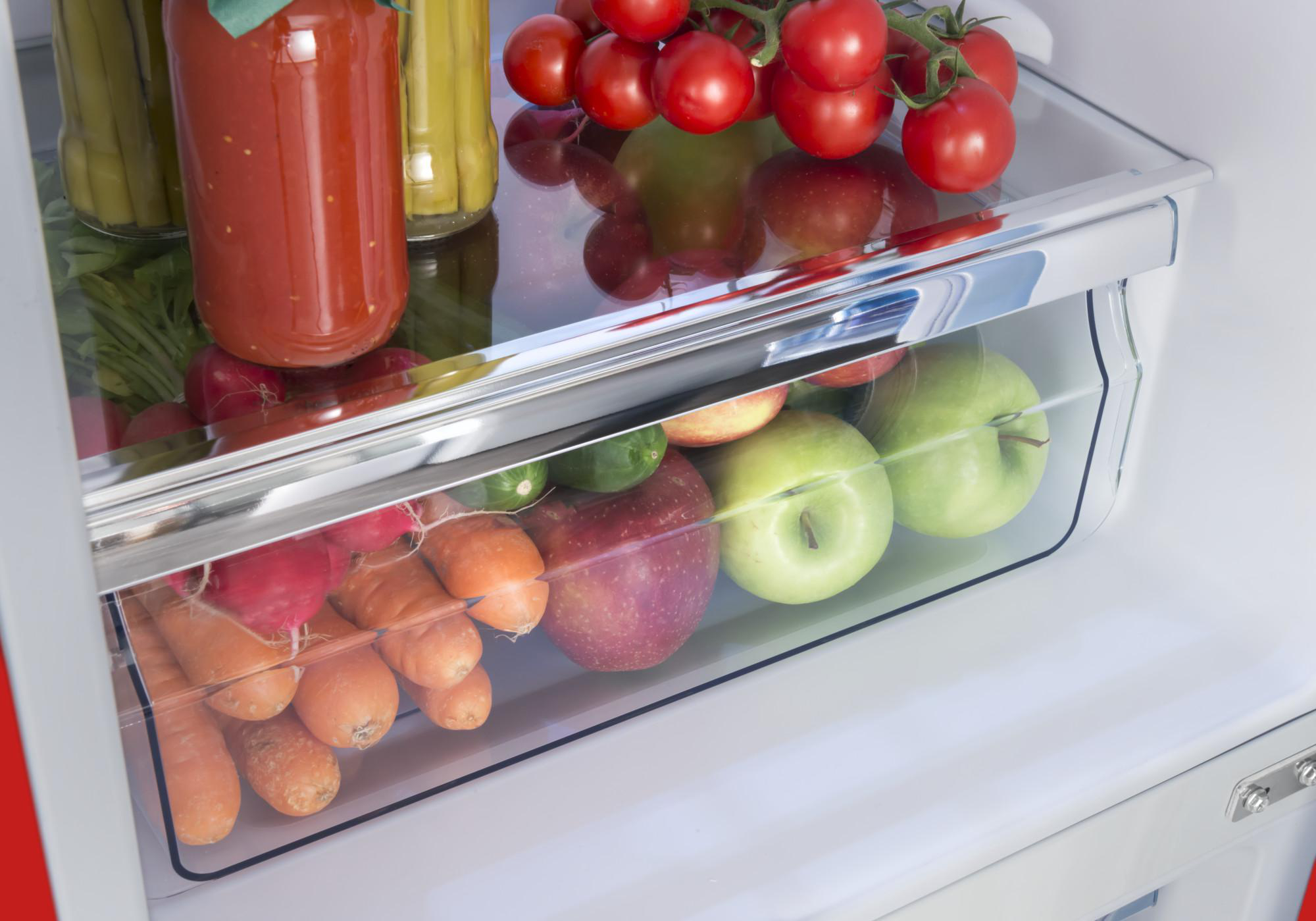 Kühlschublade mit Gemüse, Obst und Gläsern gefüllt. Glasscheibe darüber.