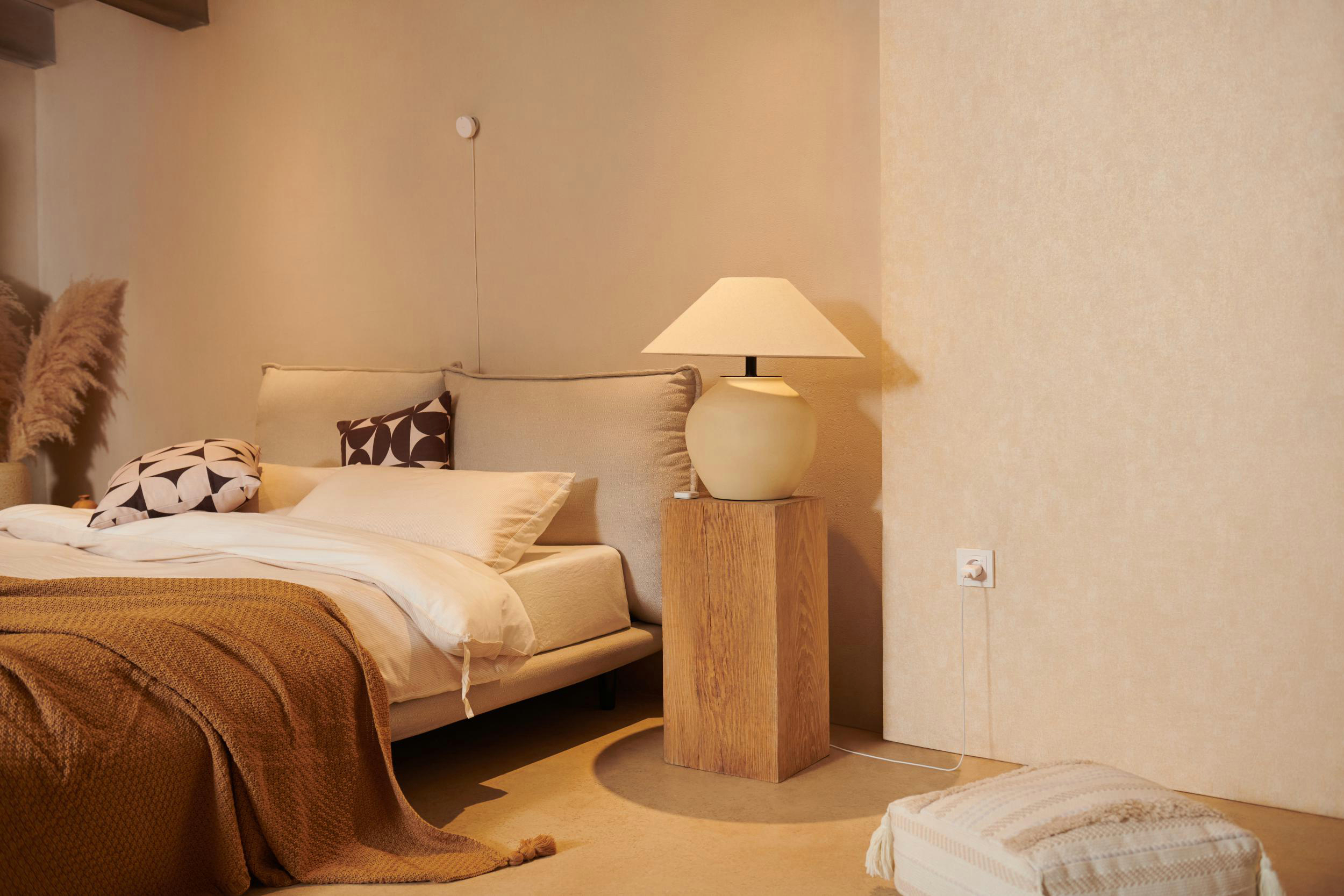 Schlafzimmer mit Bett, Lampe und Beistelltisch. Neutrales Farbschema.