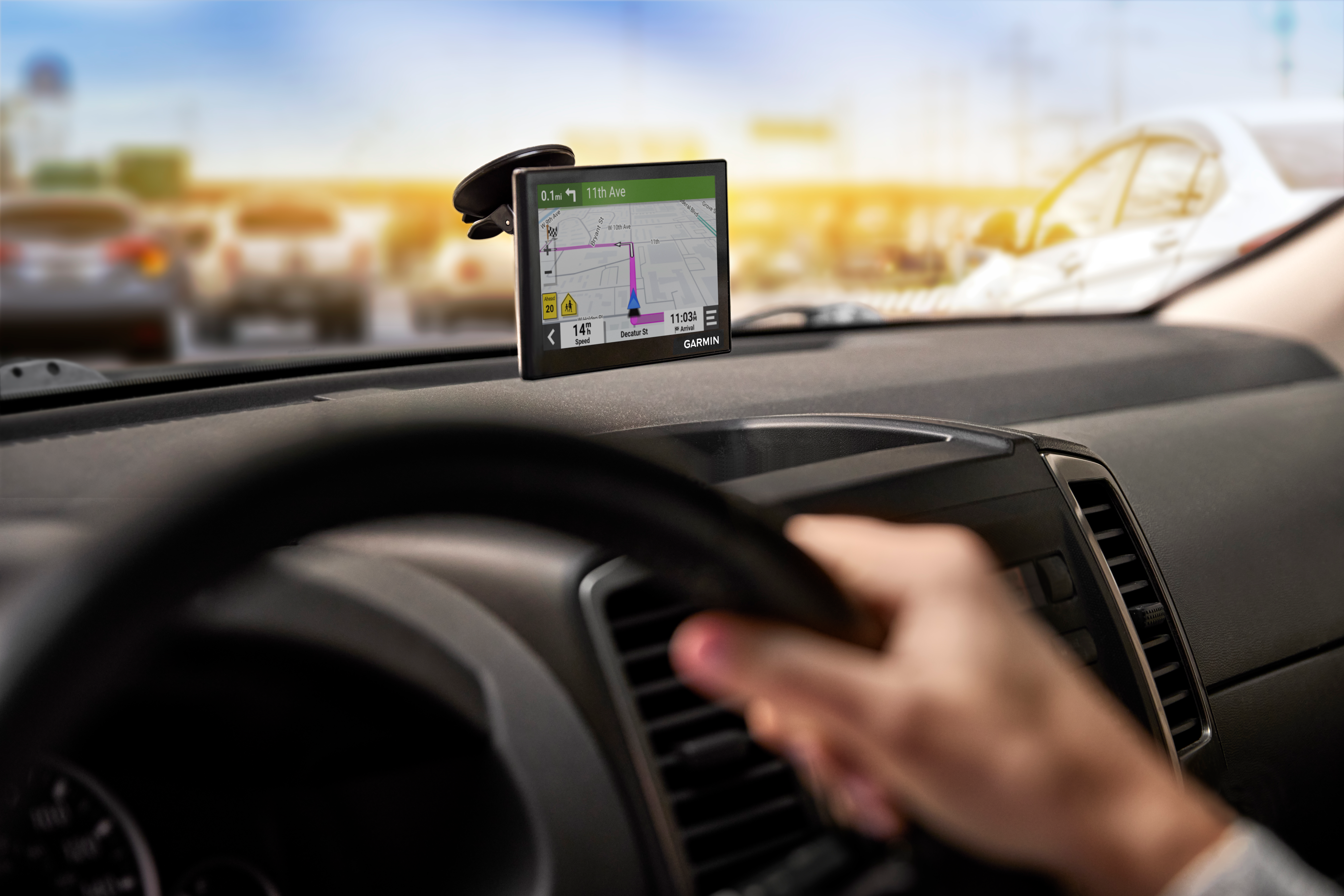 Cruscotto con dispositivo GPS. Mano sul volante, auto sullo sfondo, giornata di sole.