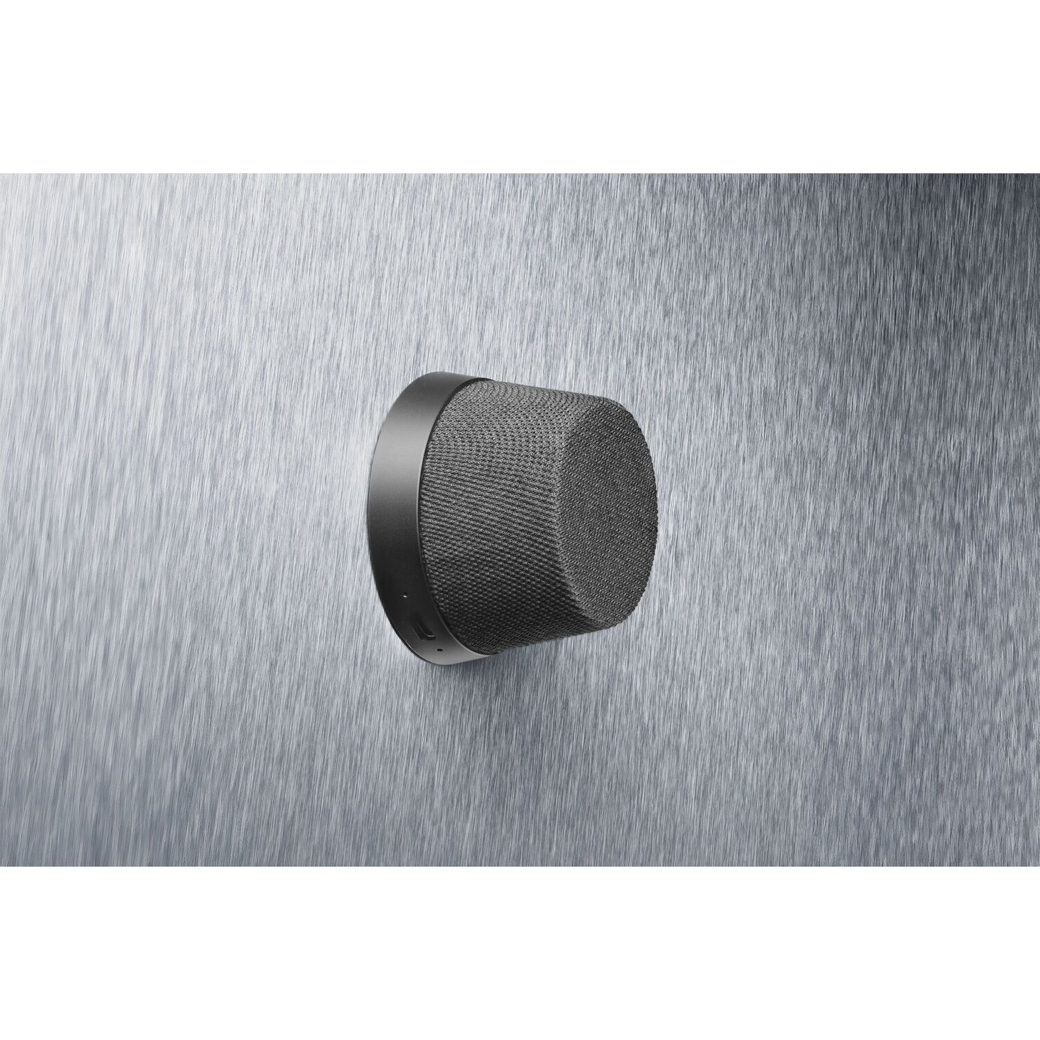 A small, black, cylindrical smart home device mounted on a textured metal surface.