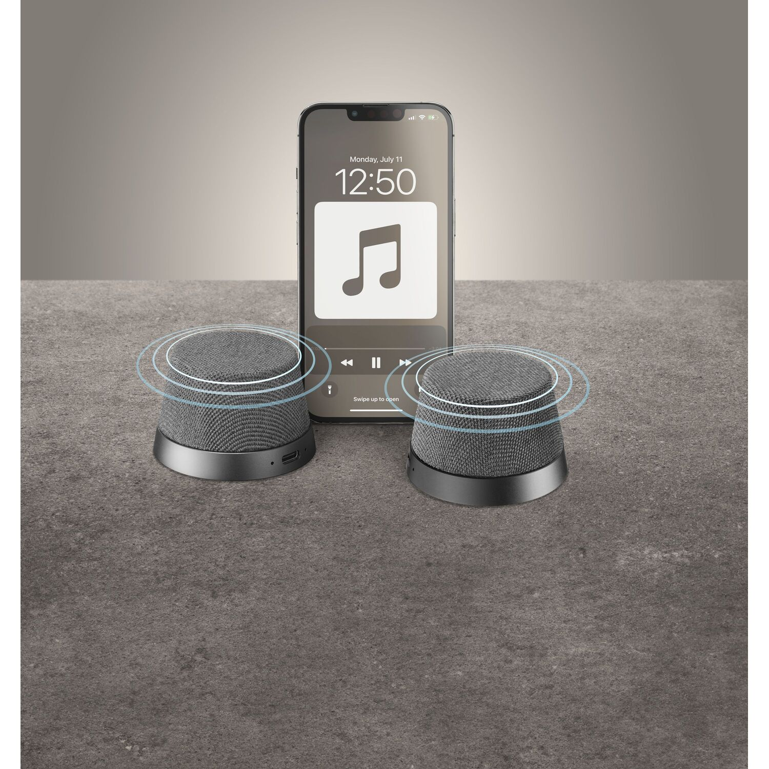 Two grey speakers with a phone in between, showing a music app interface.