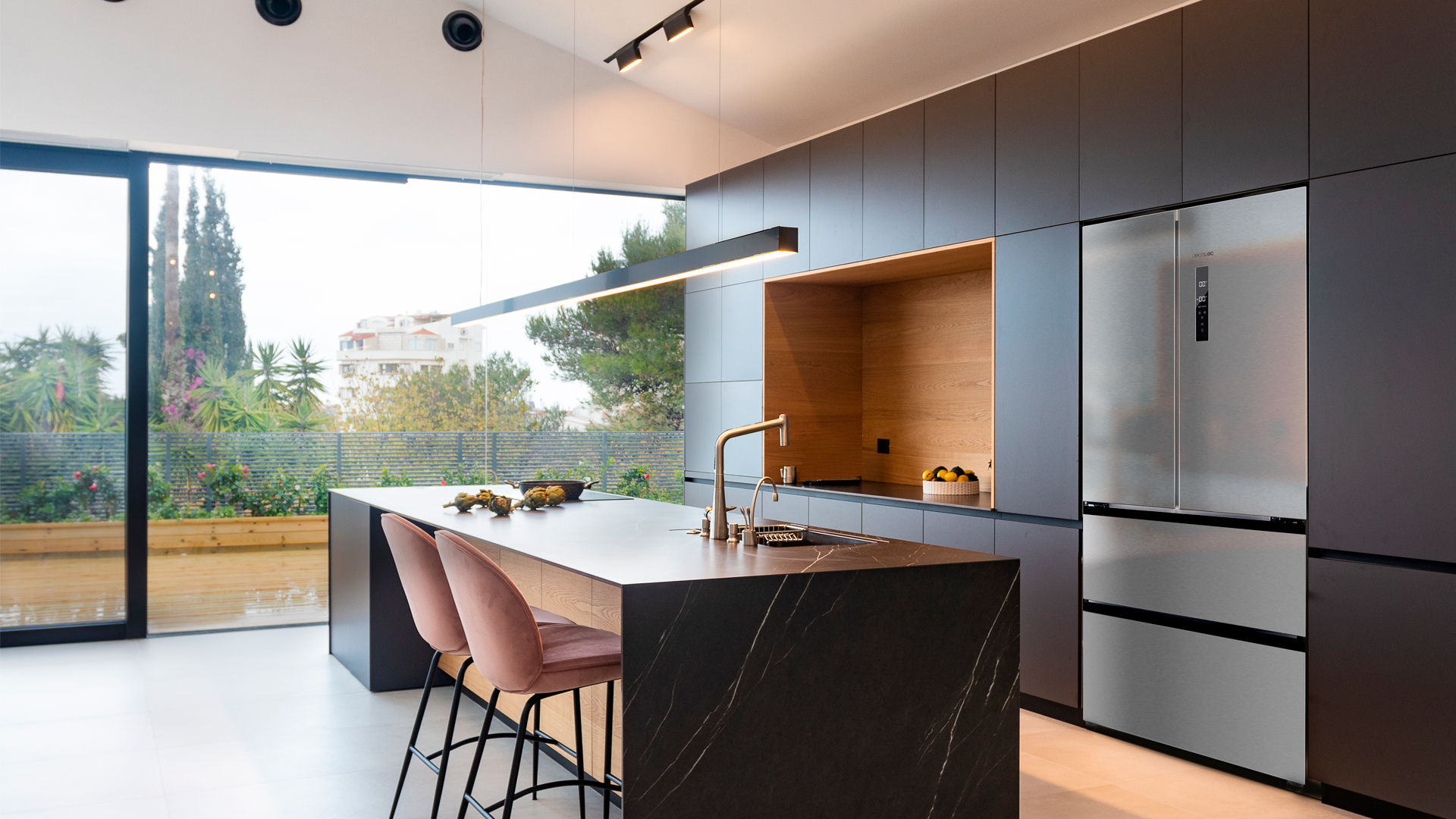Cocina moderna con isla, dos taburetes rosas, armarios oscuros y una ventana grande.
