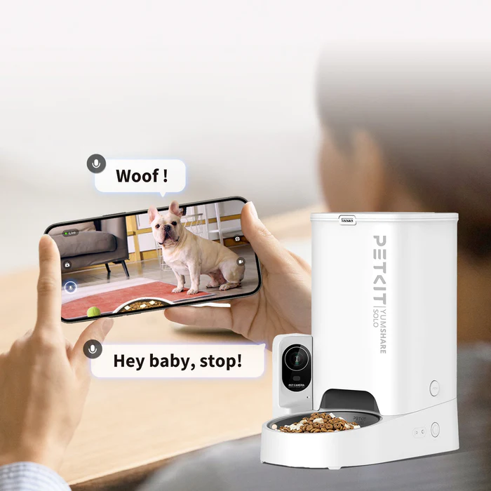 Una persona usa un telefono per nutrire un cane. Mangiatoia intelligente e cane a destra.