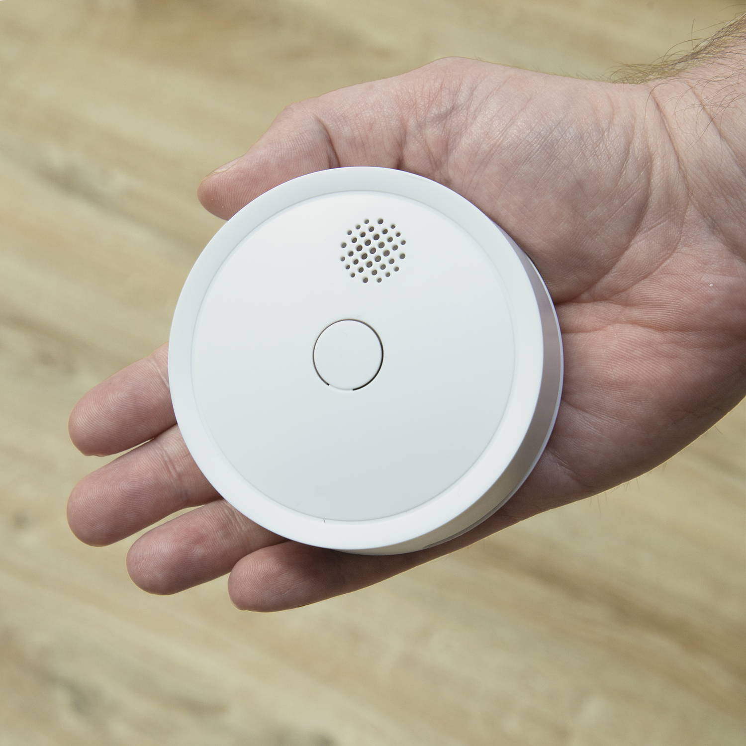 Une main tenant un détecteur de fumée blanc. L'appareil a un design circulaire.