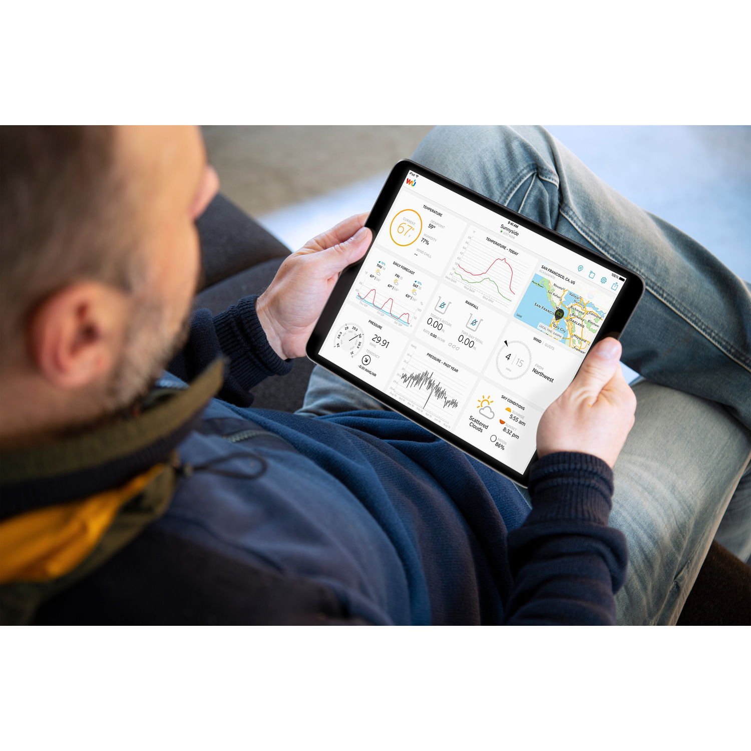 A man is holding a tablet, looking at a weather app with graphs and a map. He is wearing a jacket.