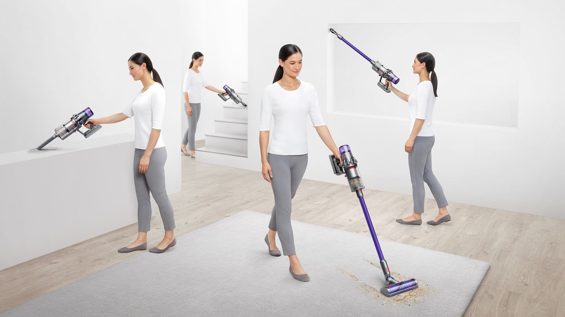 Aydınlık bir odada bir halı ve diğer yüzeylerde Dyson elektrikli süpürge kullanan bir kadın.