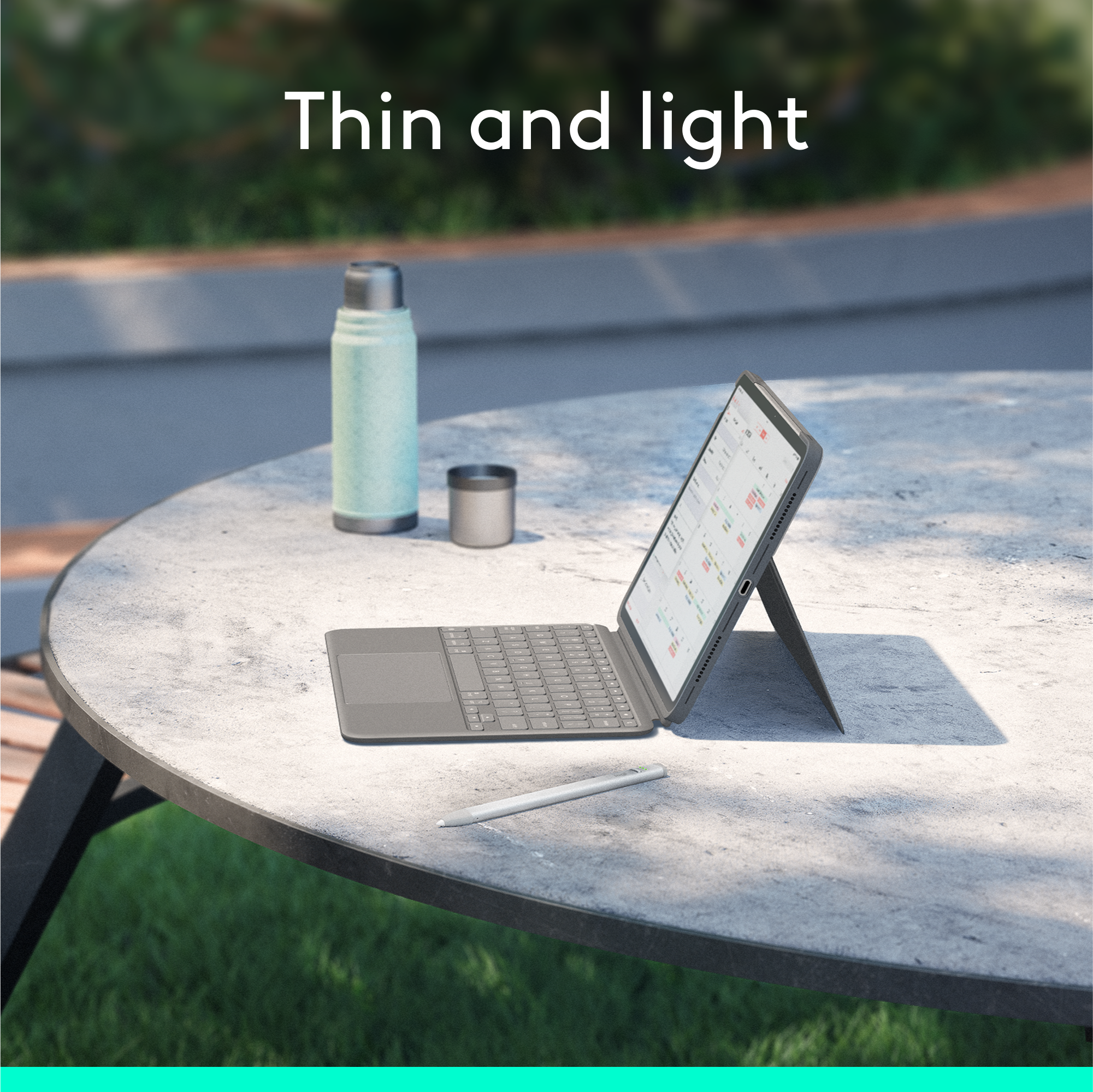 Ein Tablet mit Tastatur, ein Stift und eine Thermoskanne stehen auf einem runden Außentisch in der Sonne.