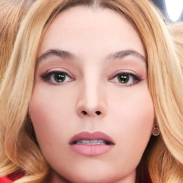 Close-up van een vrouwengezicht met blond haar, groene ogen en roze lippenstift, kijkend naar de camera.