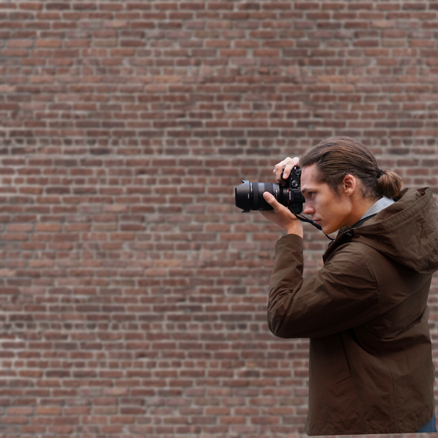 Un uomo che scatta una foto con una fotocamera, sullo sfondo di un muro di mattoni.