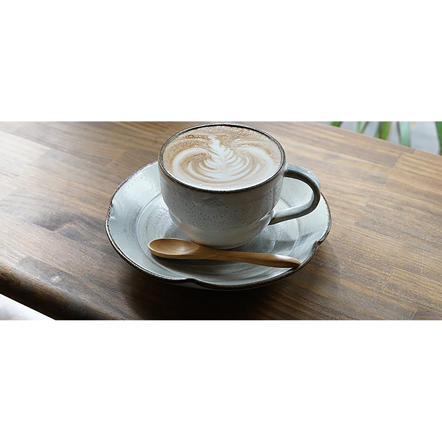 Una tazza di caffè con latte art su un piattino con un cucchiaio. Tazza e piattino sono bianchi.