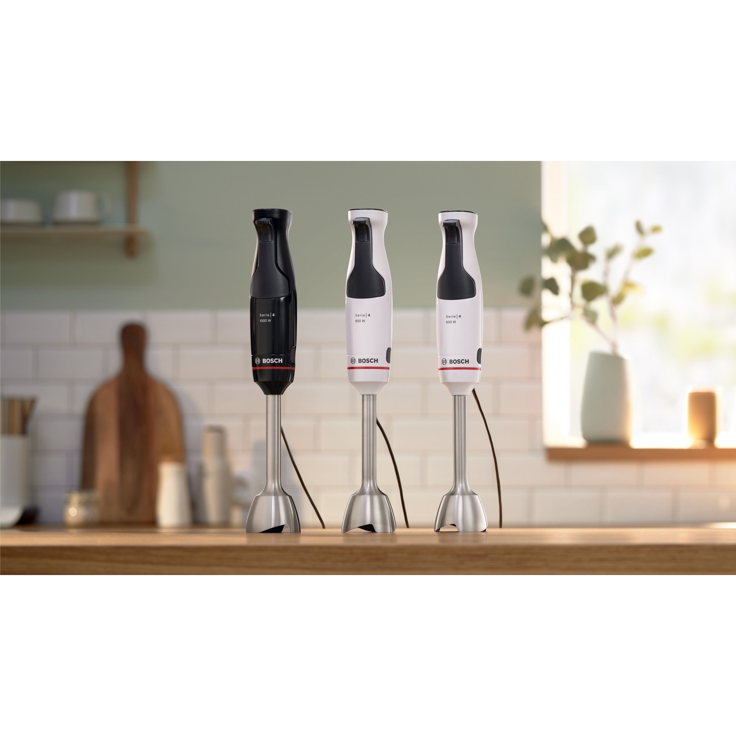 Drie Bosch staafmixers op een houten oppervlak. Eén zwart, twee wit, allemaal met roestvrijstalen mixstaven, in een keukenomgeving geplaatst.