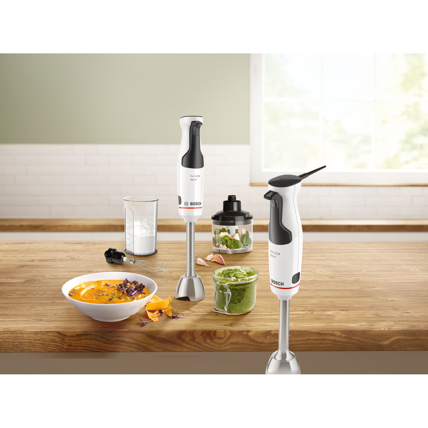 Een houten tafel met een soepkom, blenders, ingrediënten en een glas. Natuurlijk licht verlicht de scène.