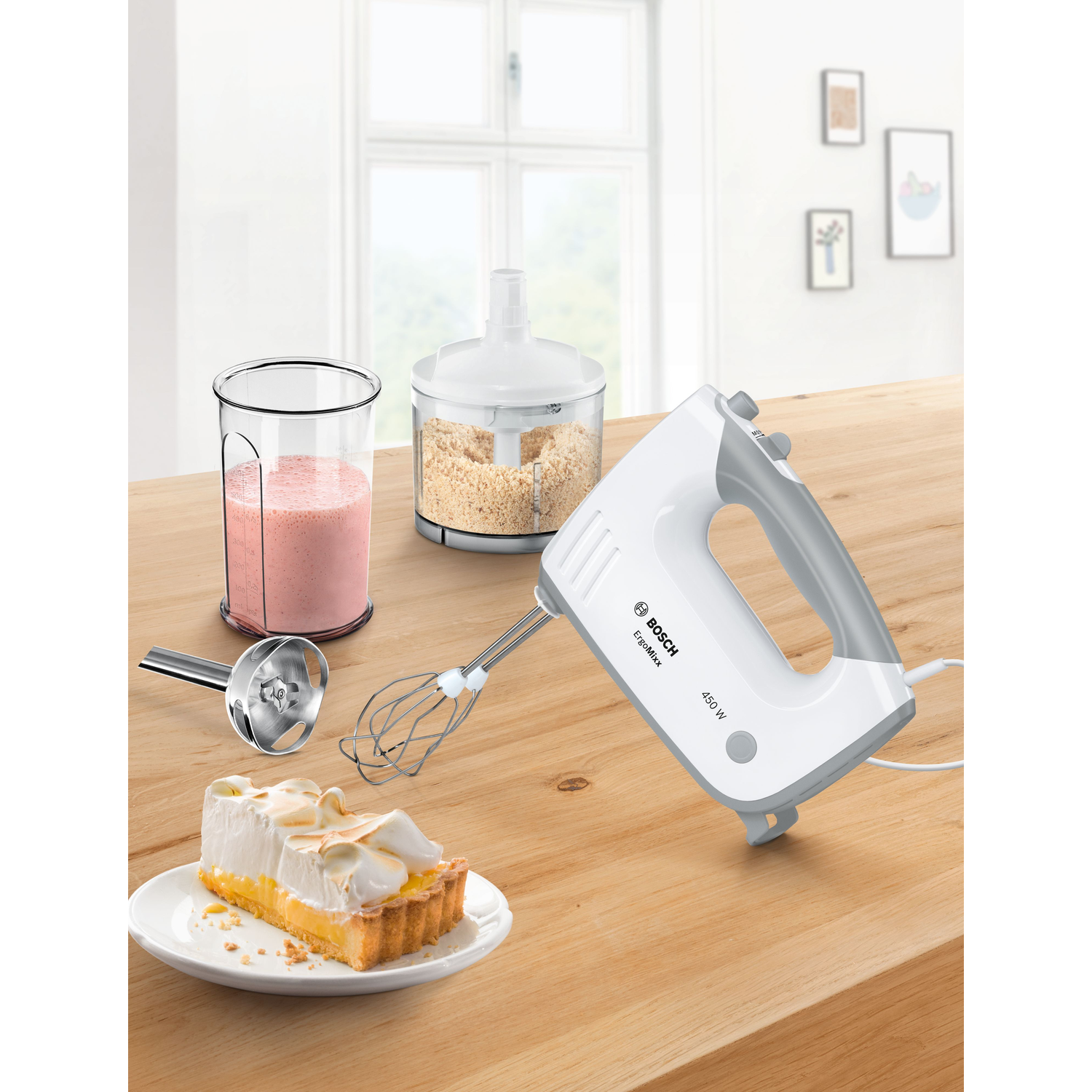 A hand mixer, glass with pink liquid, and a tart with a slice on a wooden table.