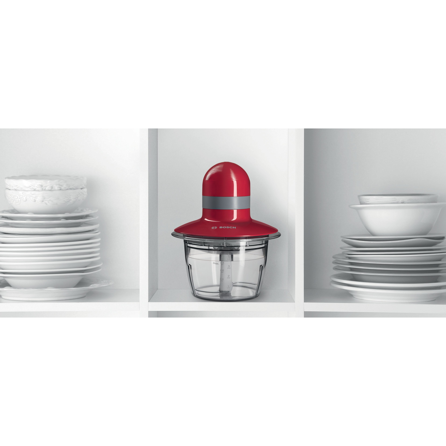 A red and gray food processor. It is sitting in a white shelf between dishes.