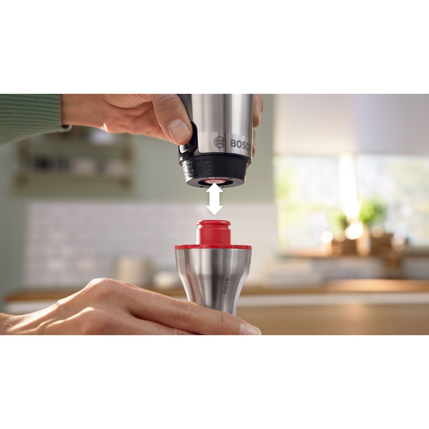 Hands assembling a stainless steel blender with a red base.