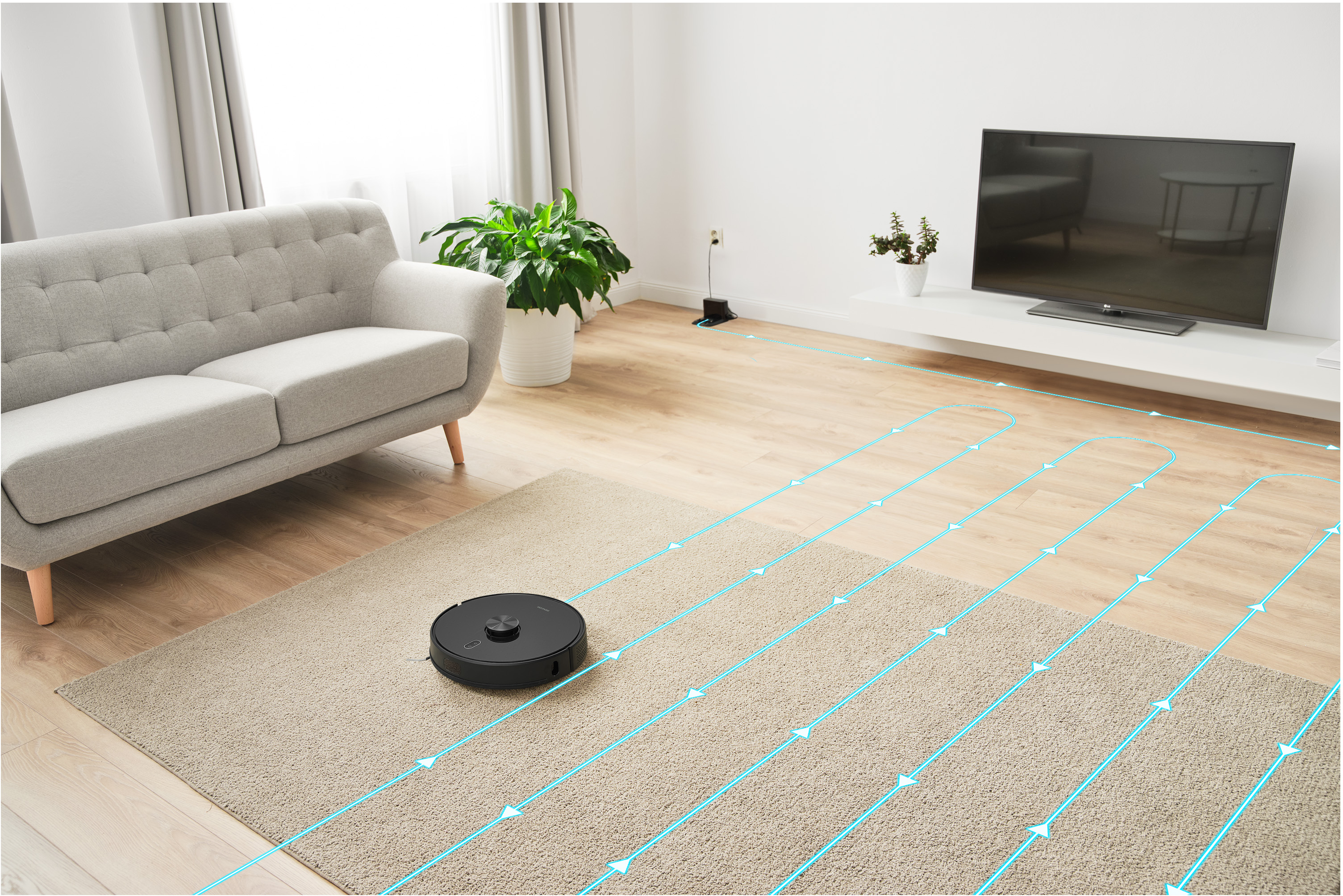 Fekete robotporszívó szőnyegen, tisztítási útvonalvonalakat mutatva. Kanapé és TV a háttérben.