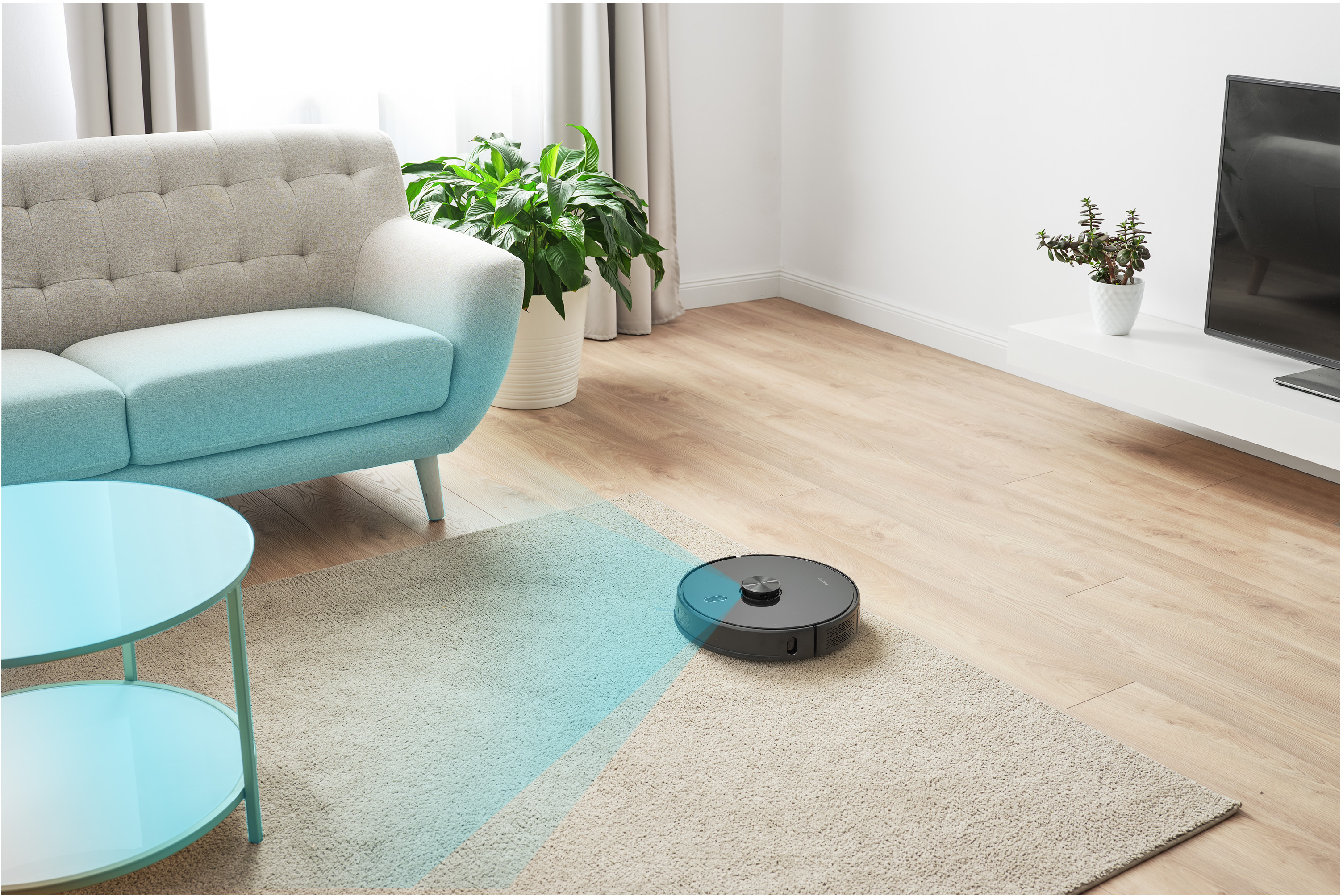 Egy robotporszívó takarít egy szobát. Egy kanapé, egy szőnyeg és egy asztal látható.