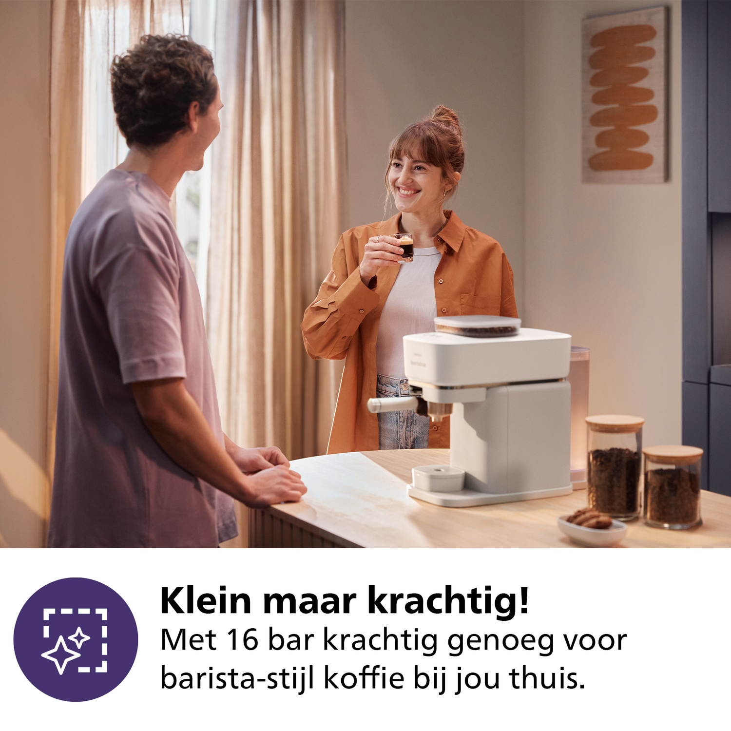 A couple in a kitchen, one holding a coffee cup, with a white coffee machine. Text: Klein maar krachtig!
