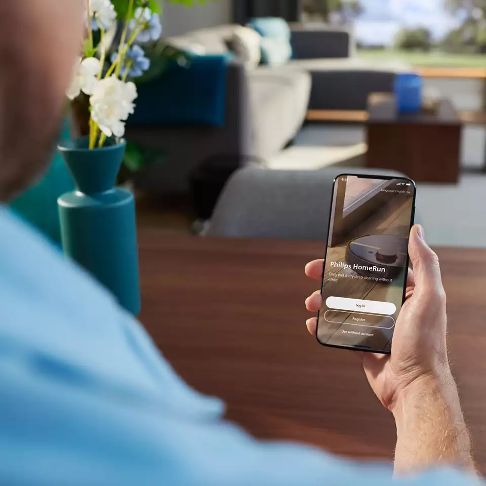 Osoba trzymająca telefon, pokazująca aplikację Philips HomeRun. Ekran wyświetla opcje logowania i rejestracji.