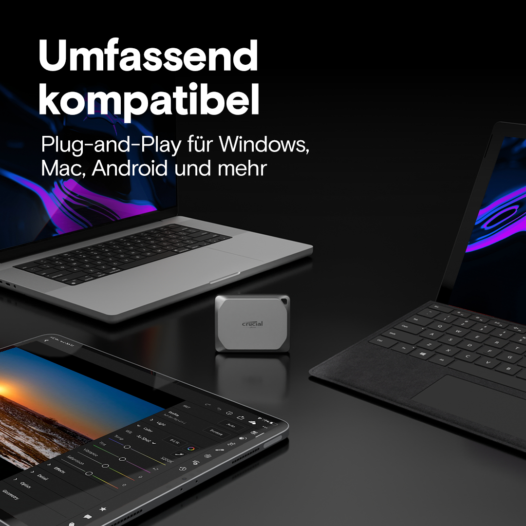Laptops, Tablet und ein silbernes Crucial-Gerät auf dunkler Oberfläche. Der Text lautet 'Umfassend kompatibel'.